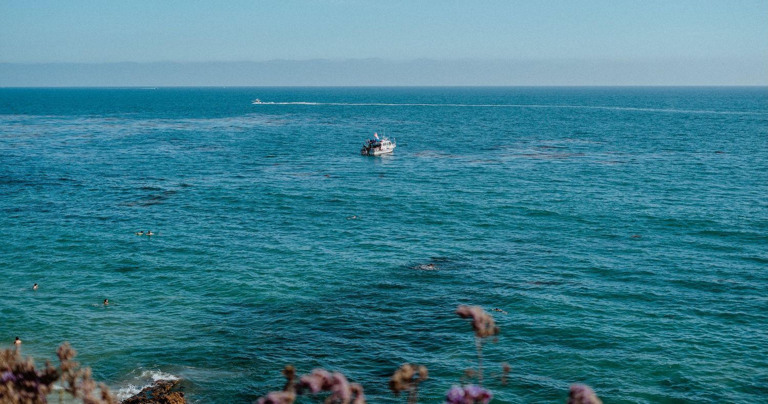 Small white boat sailing on calm turquoise ocean water under clear blue sky.