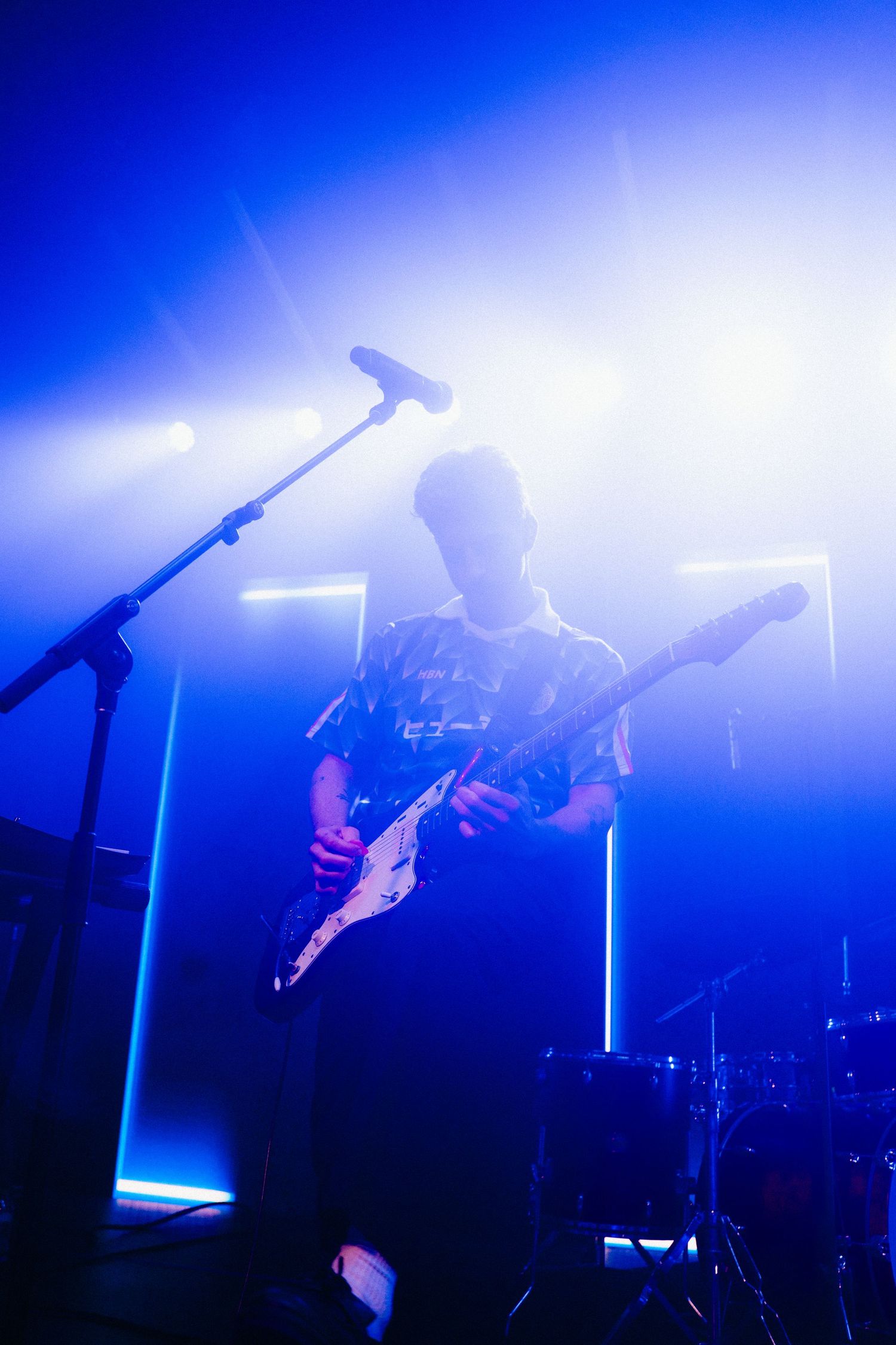 A musician plays an electric guitar against a hazy blue background.