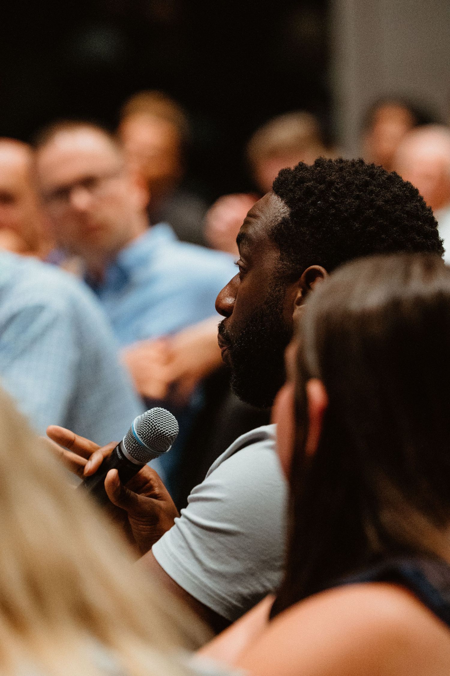 A bearded Black man holds a microphone at a crowded event, speaking during a Q&A session.