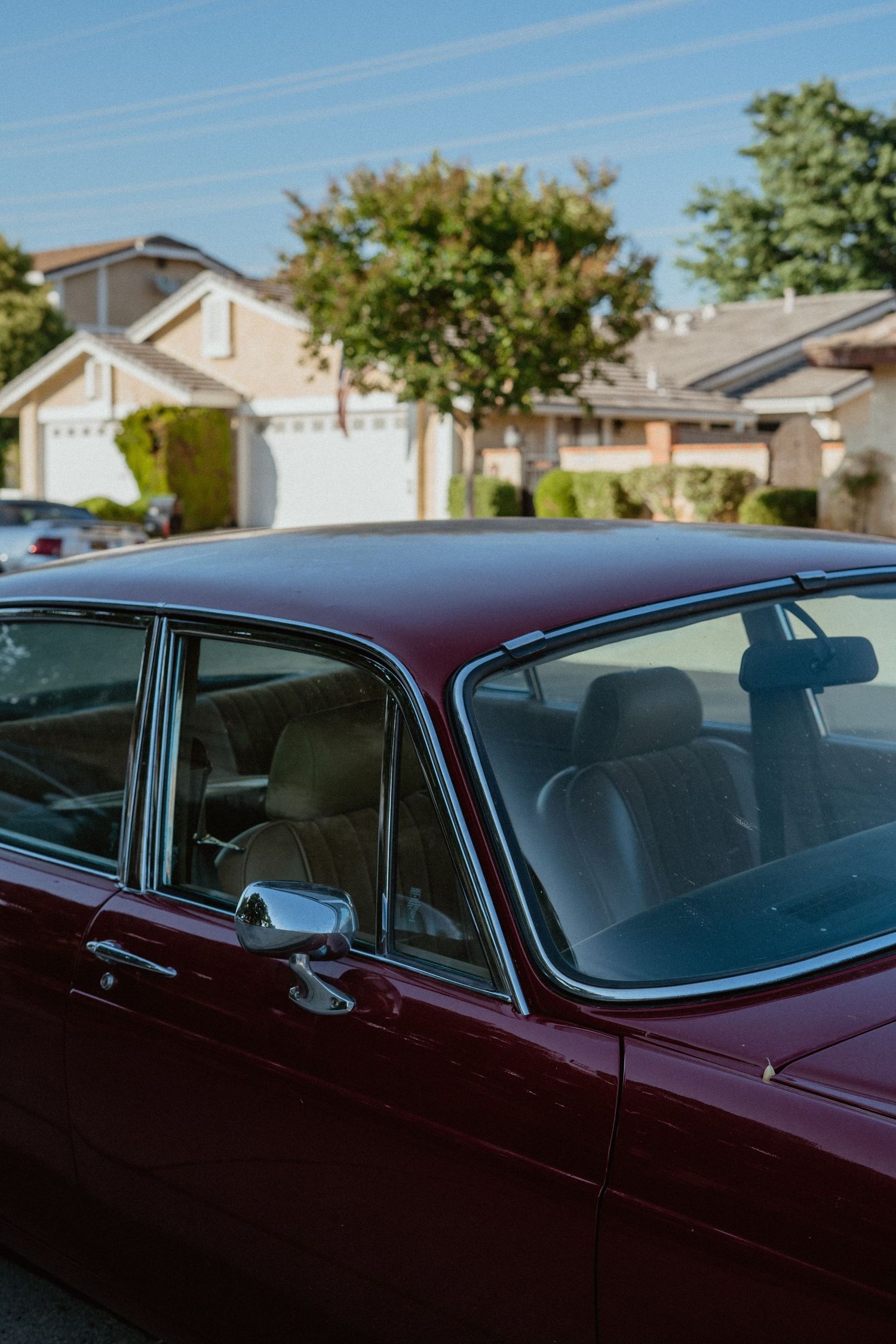 A classic burgundy vintage car parked on a suburban street with houses and trees in the background.