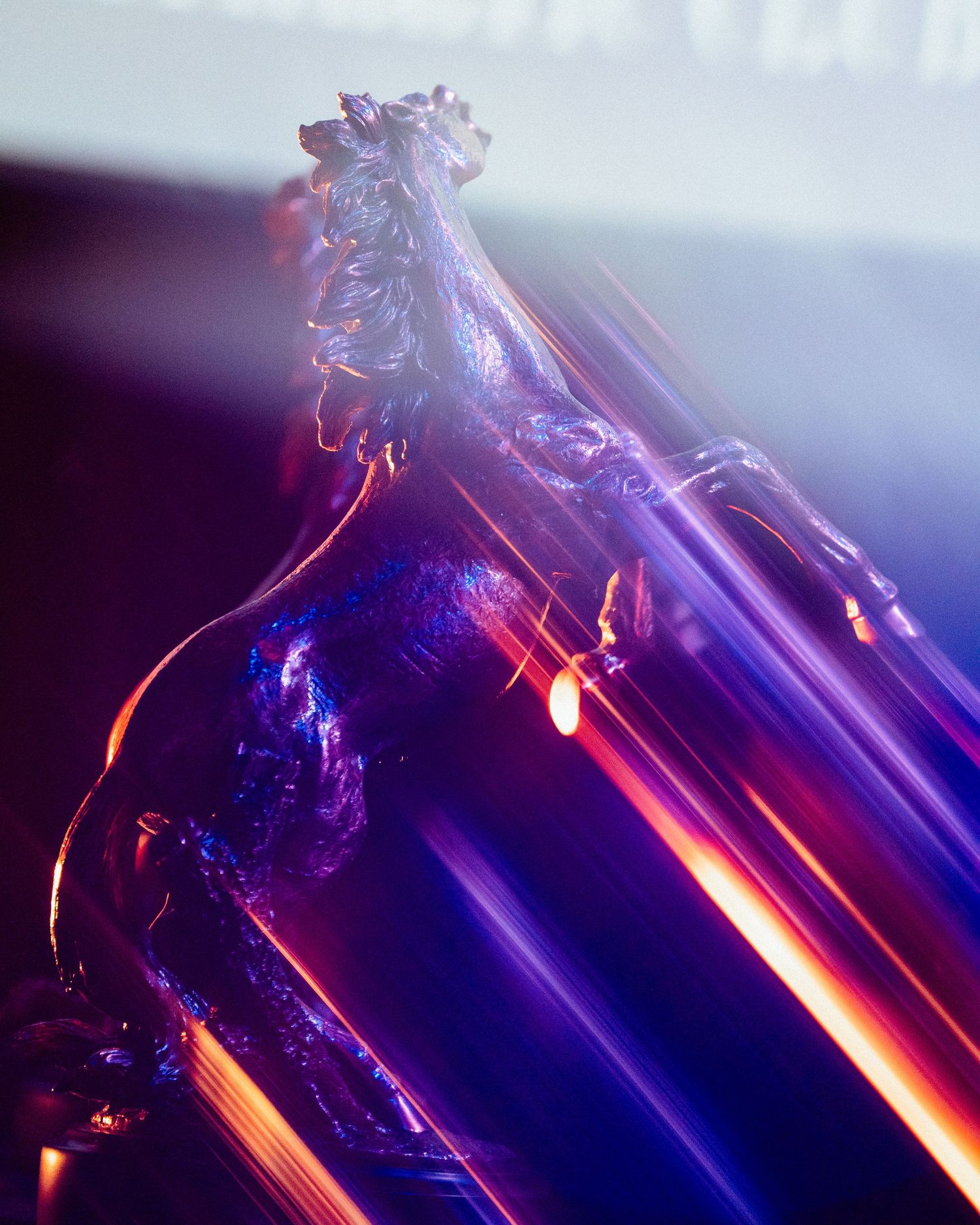 Glass horse sculpture with vibrant purple and orange light streaks creating a dynamic, artistic display.