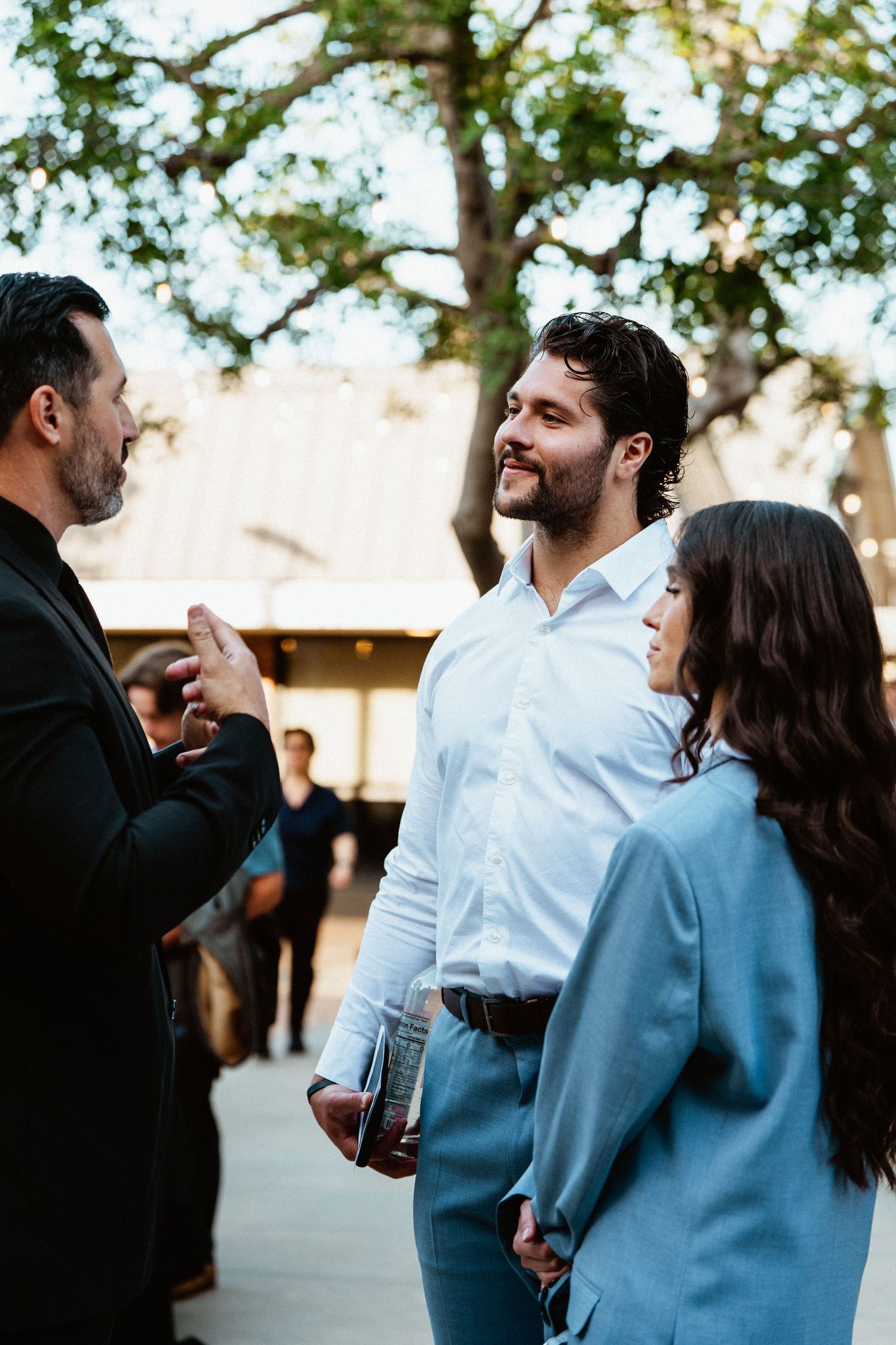 Three professionals networking outdoors at an event, smiling and conversing near trees.