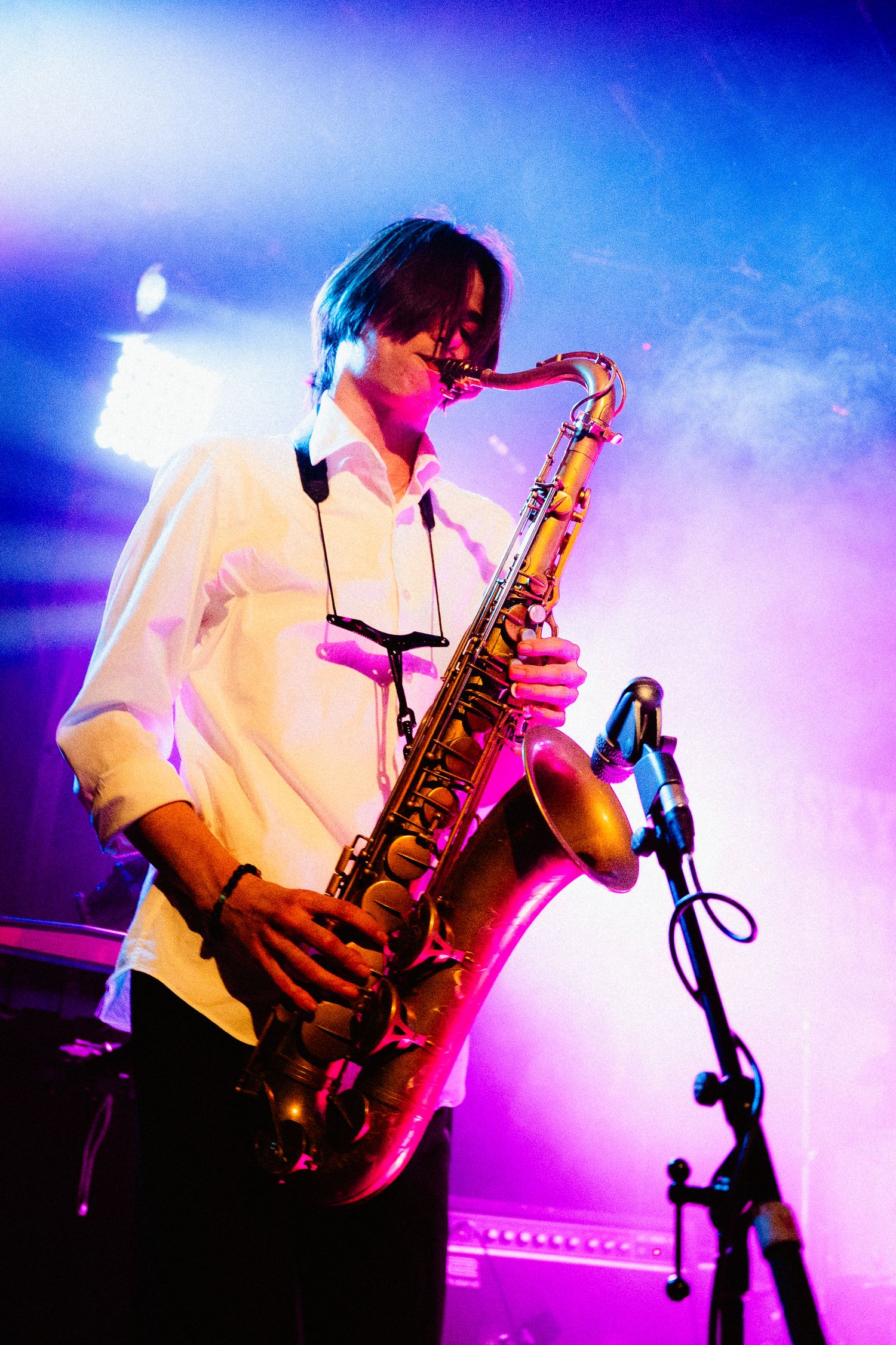 A musician in a white button up shirt plays a saxophone against a blue and purple background.