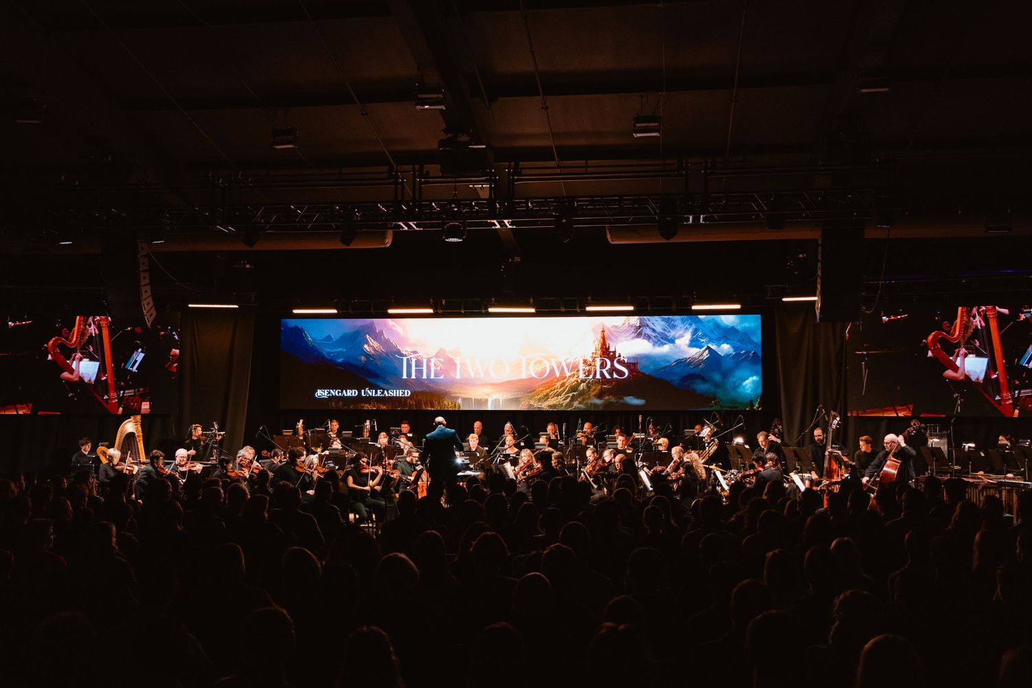 Full orchestra performing on stage before a large audience in a dark venue.