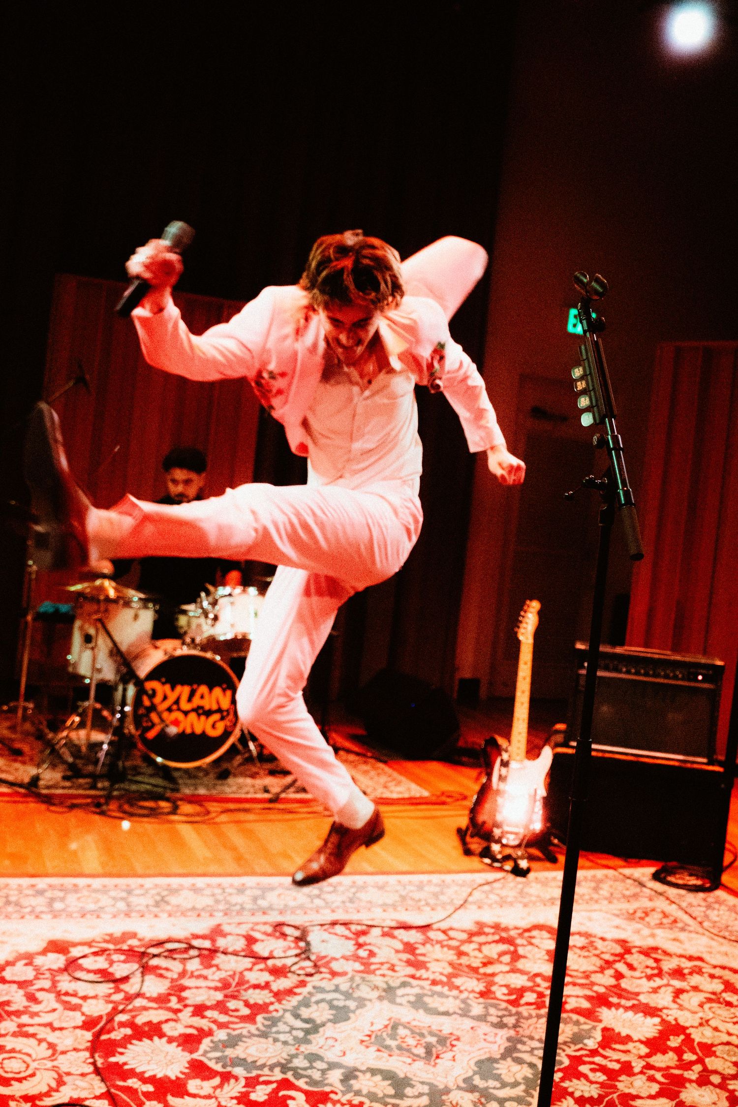 Energetic male performer in white suit jumping on stage at Dylan Yong concert under red lights.
