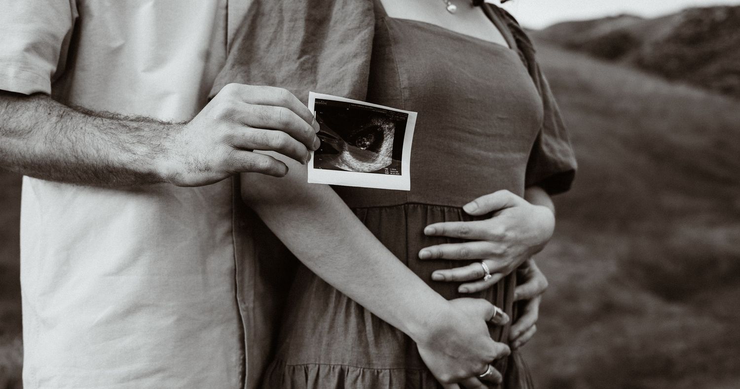 Black and white photo of couple holding ultrasound scan together outdoors in nature.