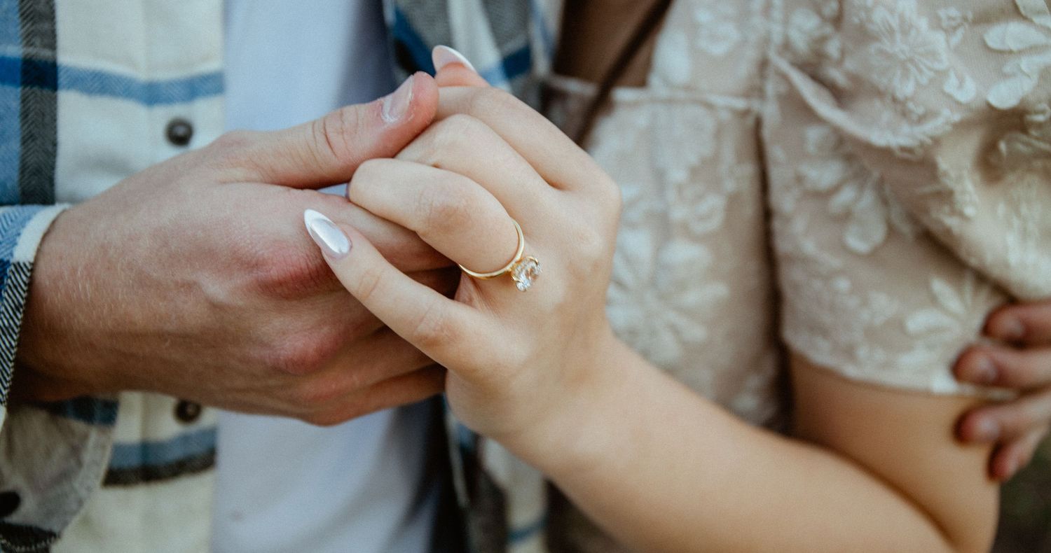 Close-up of couple holding hands with gold engagement ring on woman's finger.