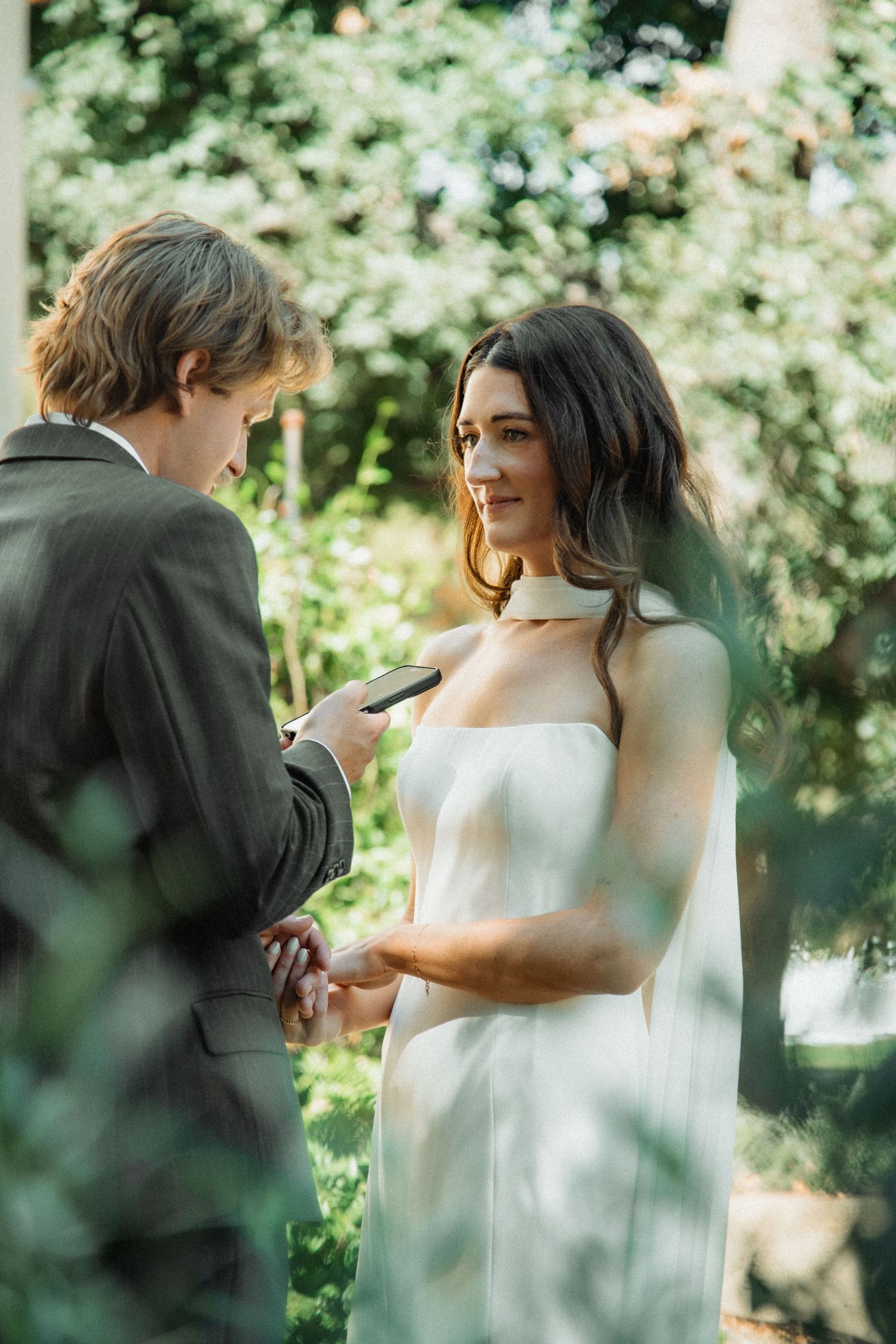 Groom reading wedding vows to emotional bride in white gown surrounded by lush green garden.