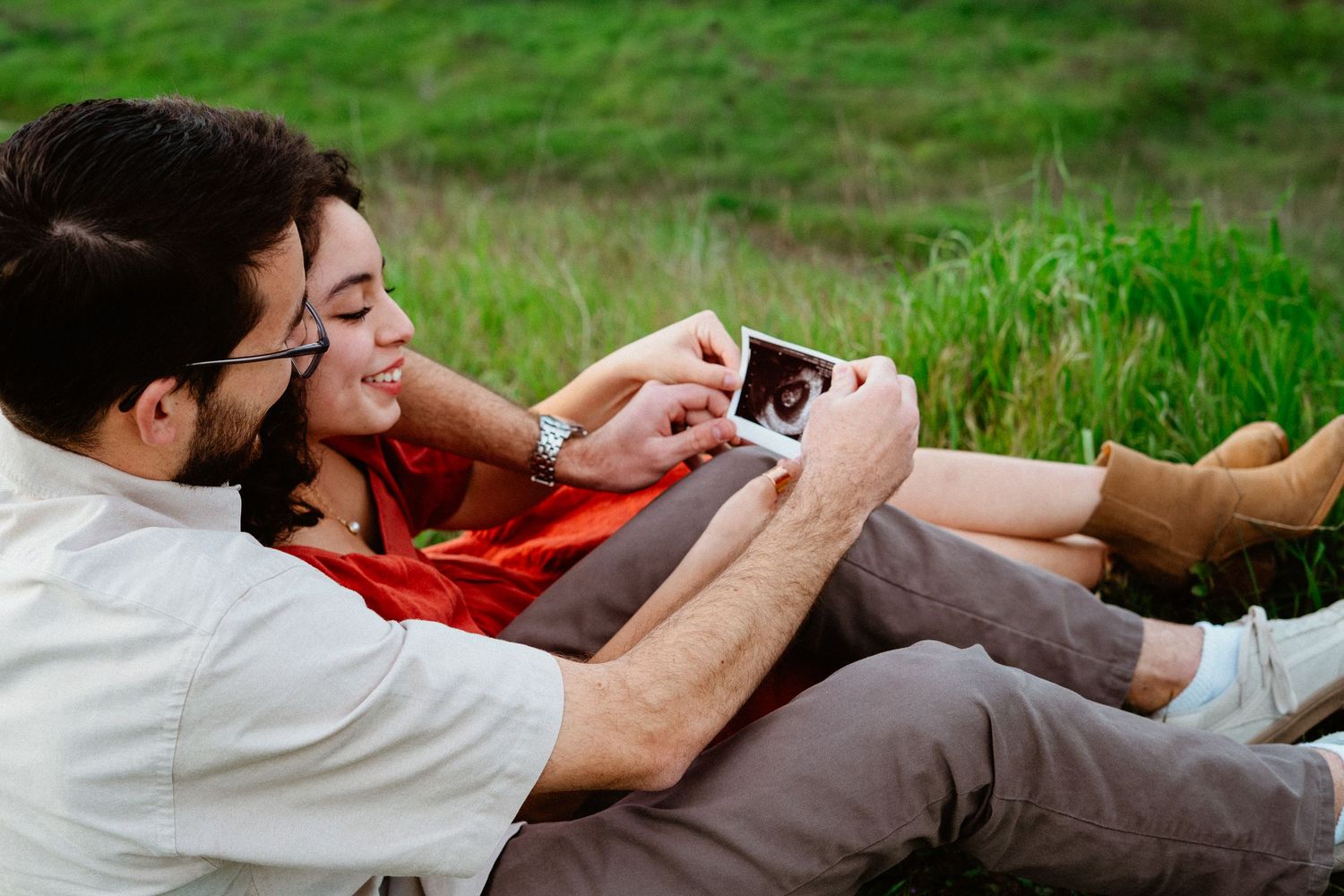 Couple lying on grass looking at ultrasound photo together.