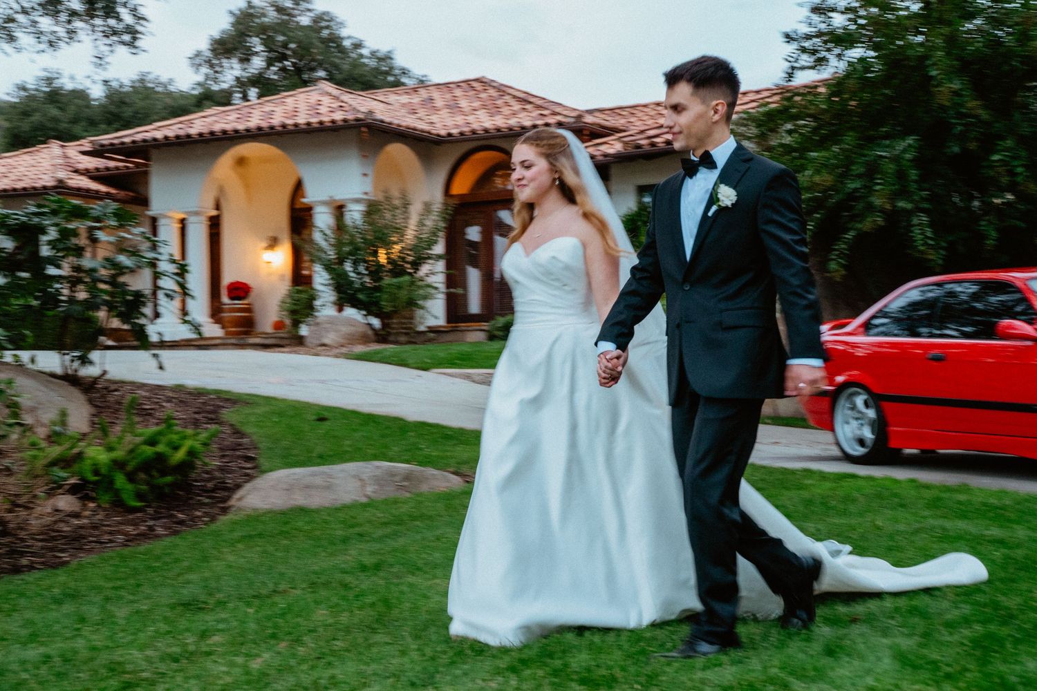 Bride and groom walking hand in hand outside a Spanish-style villa on their wedding day.
