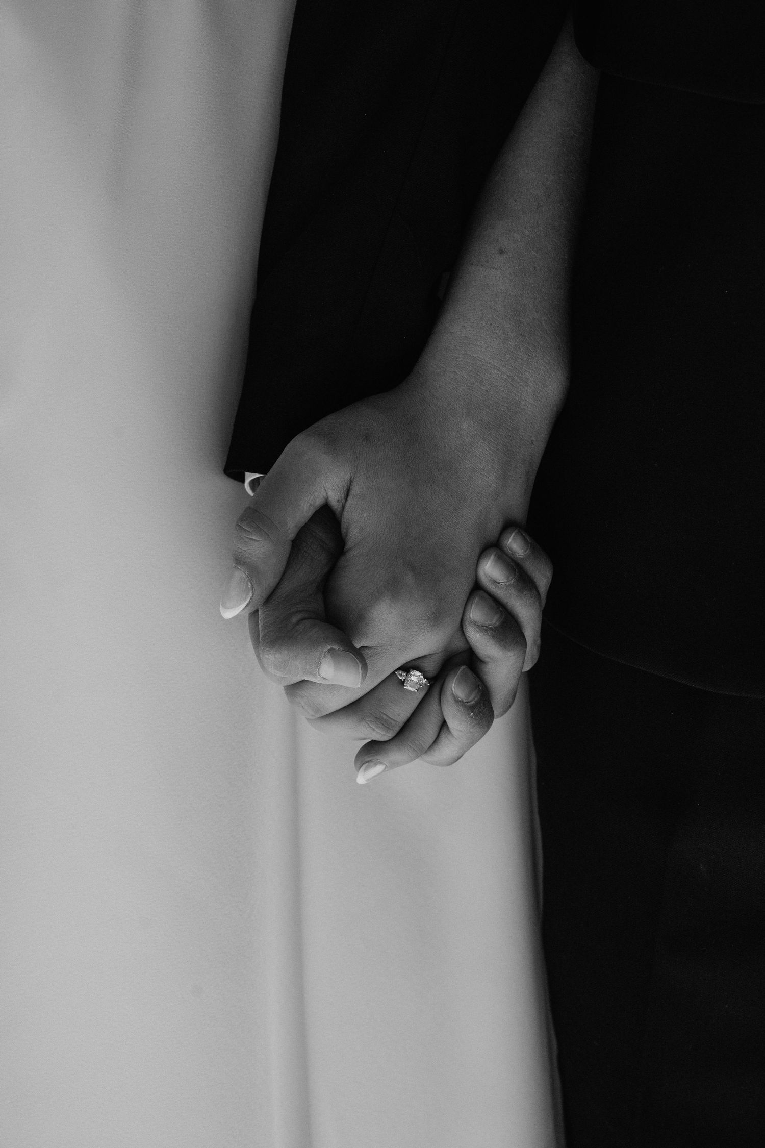 Black and white close-up of bride and groom holding hands, showcasing elegant engagement ring.