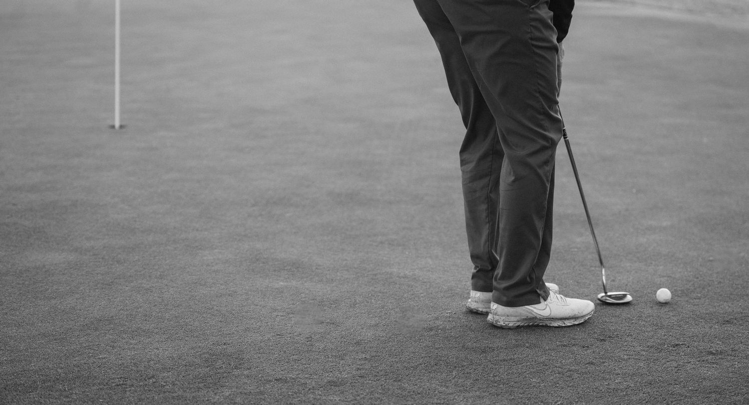 Black and white photo of golfer putting on green near flag hole on manicured golf course.