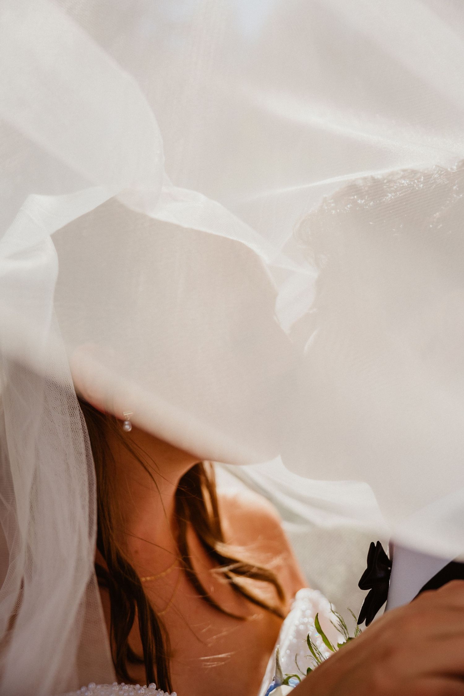 Bride and groom sharing a kiss under flowing white wedding veil, romantic close-up detail shot.
