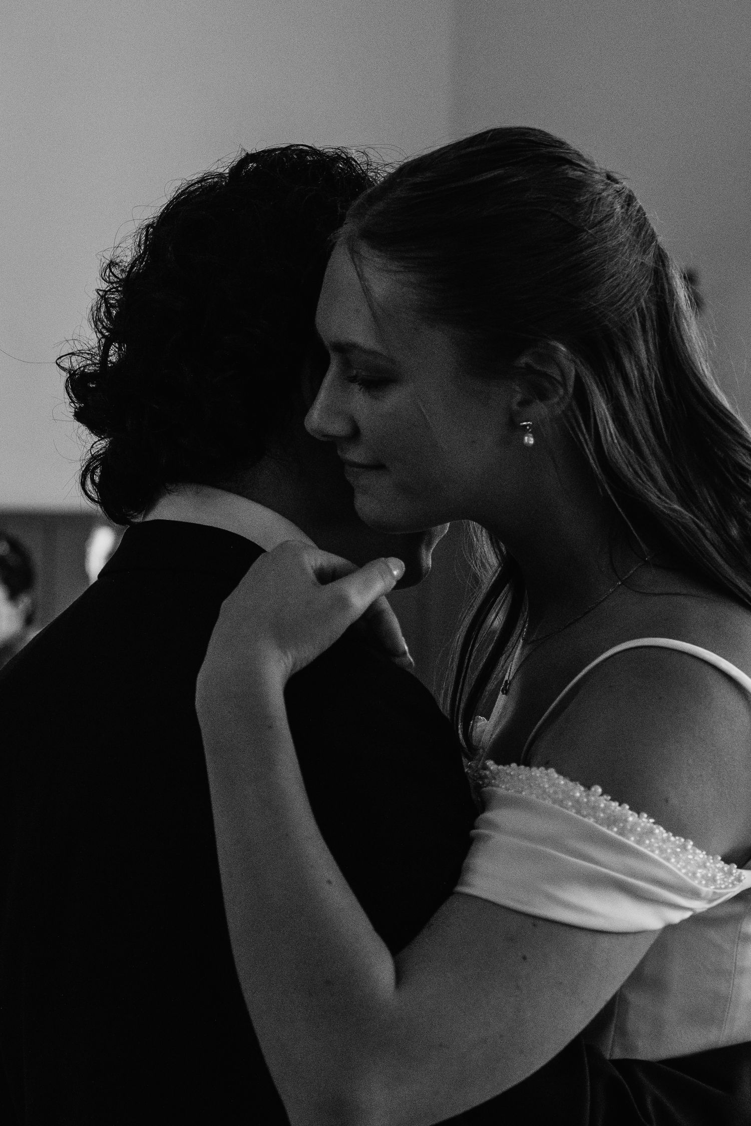 Black and white photo of a couple sharing an intimate dance, woman in off-shoulder dress embracing partner tenderly.