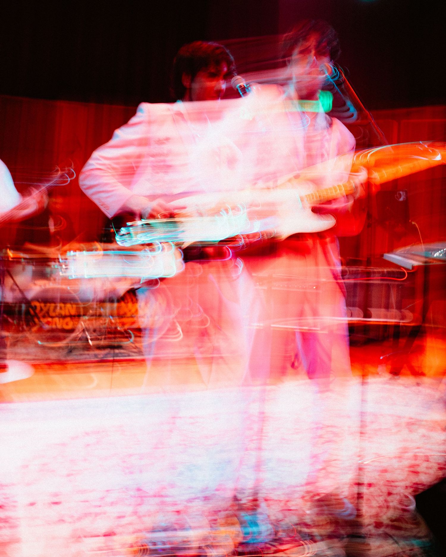 Abstract long exposure photo of wedding band musicians performing with electric guitar under red stage lights.
