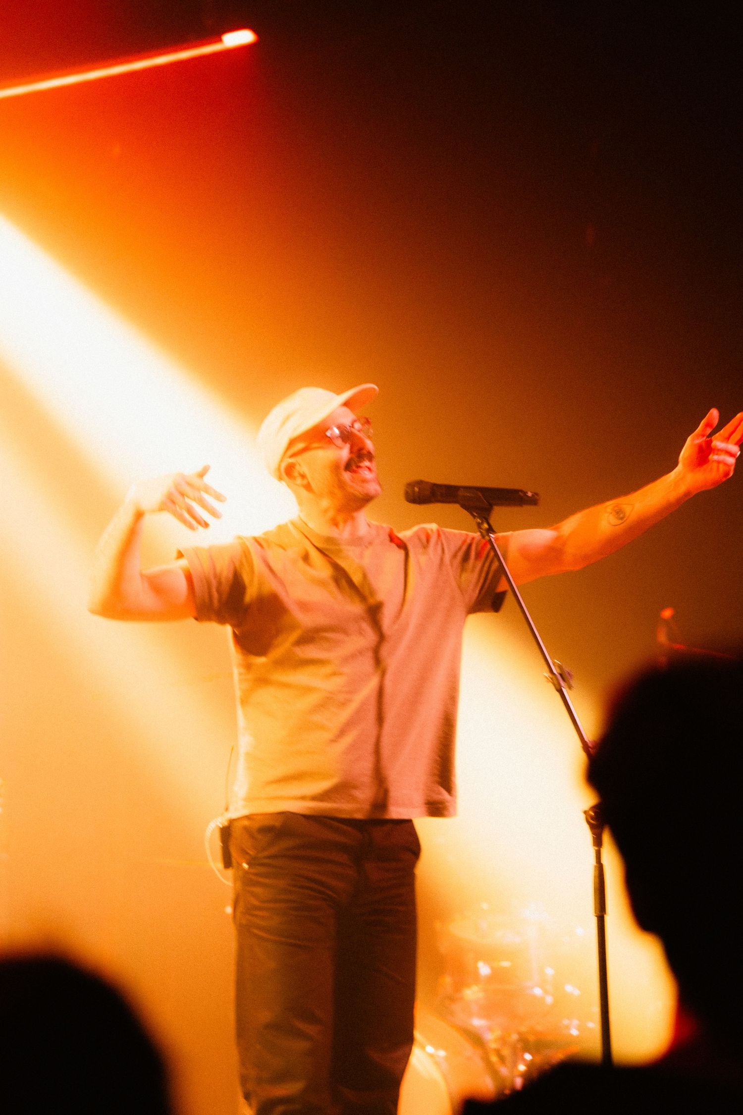 Energetic male singer performing on stage under warm golden spotlight wearing a white cap.
