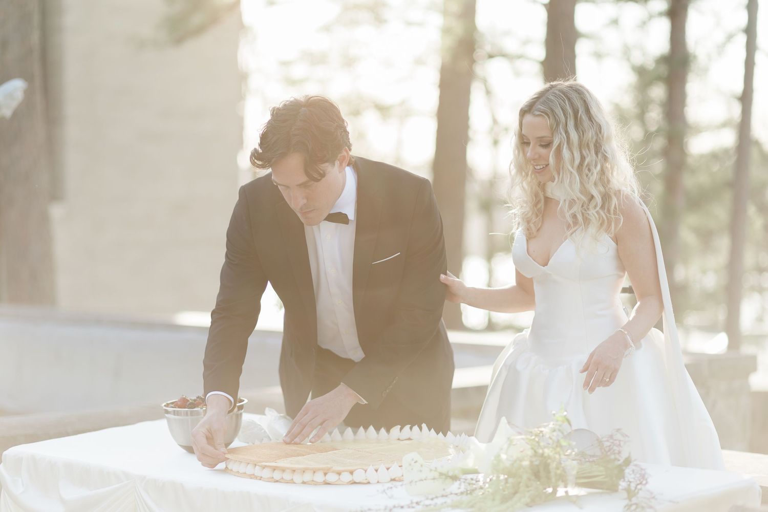 Bride and groom at cake table in front of mansion with sunset.
