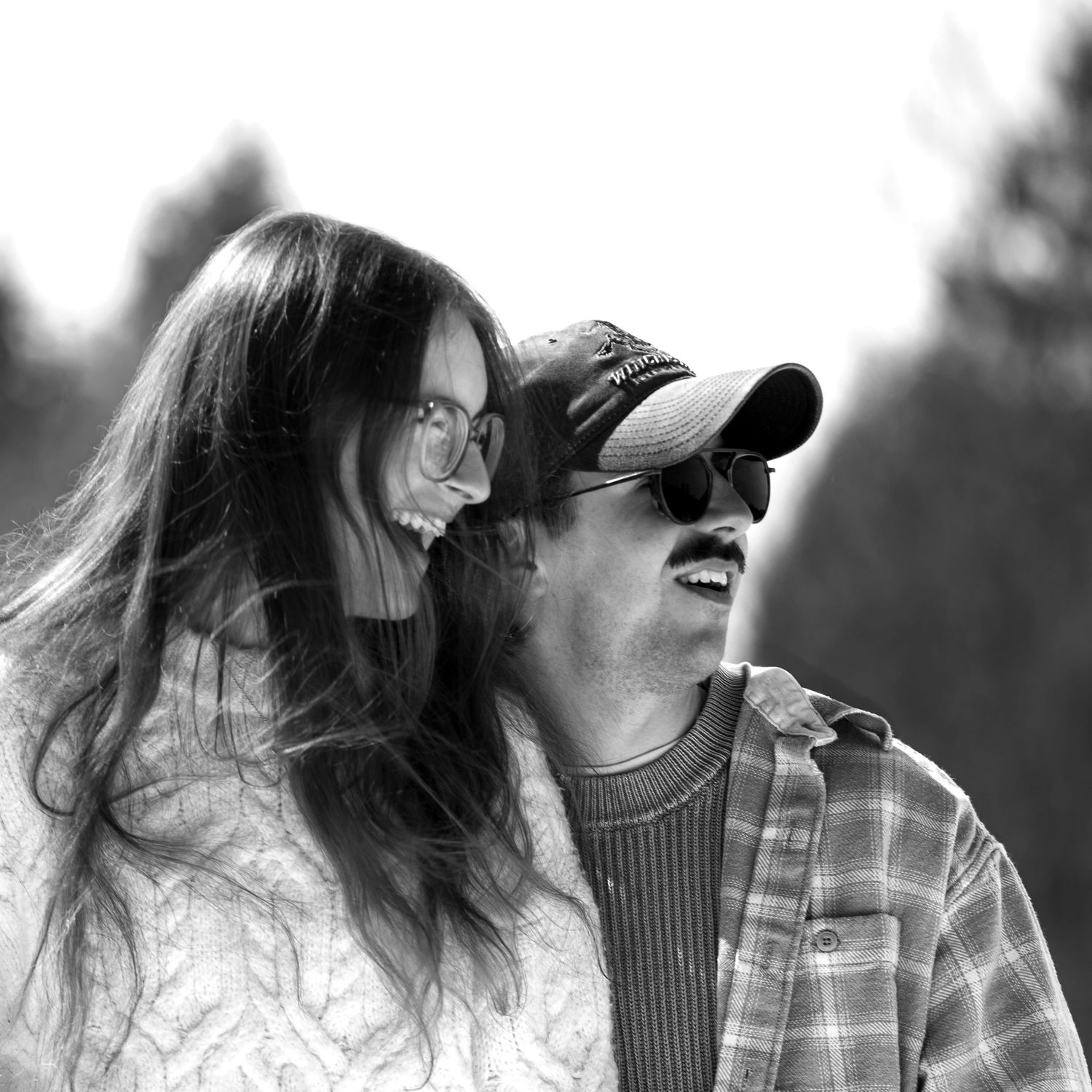 Black and white photo of a happy couple laughing together outdoors, woman in sweater and man in cap.