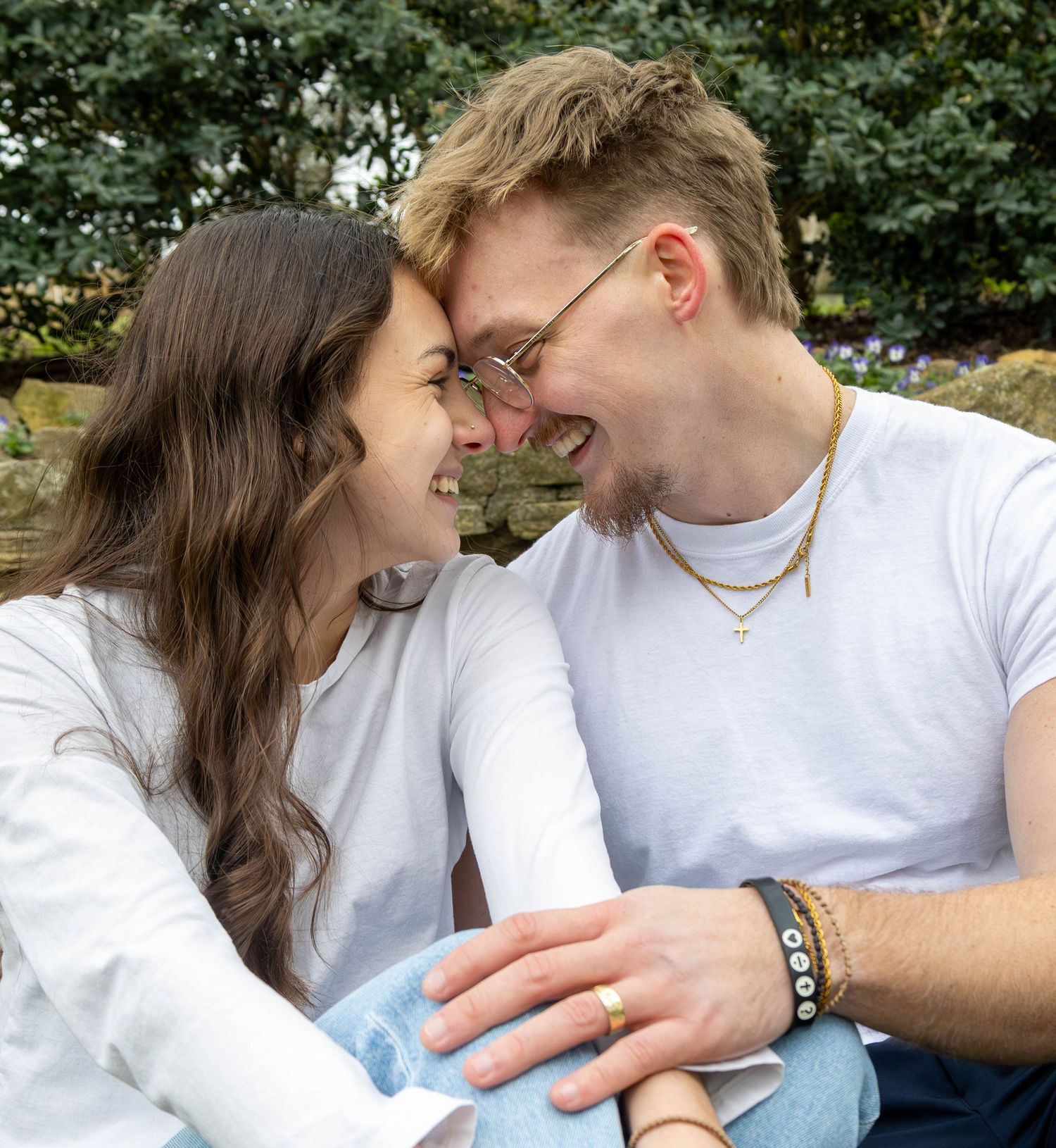 A happy young couple laughing and touching foreheads outdoors in a garden setting.