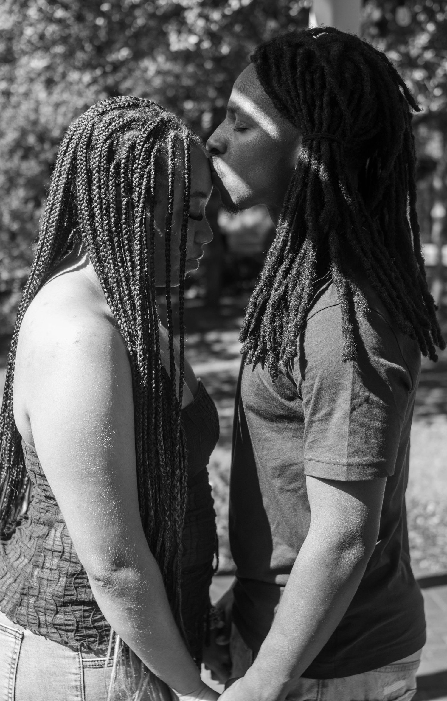 Black and white photo showing two people with long braids and dreadlocks standing close together outdoors.
