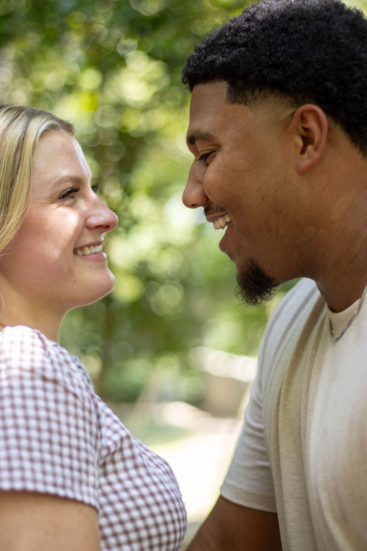 A couple shares a romantic moment outdoors with natural bokeh lighting and green foliage in the background.