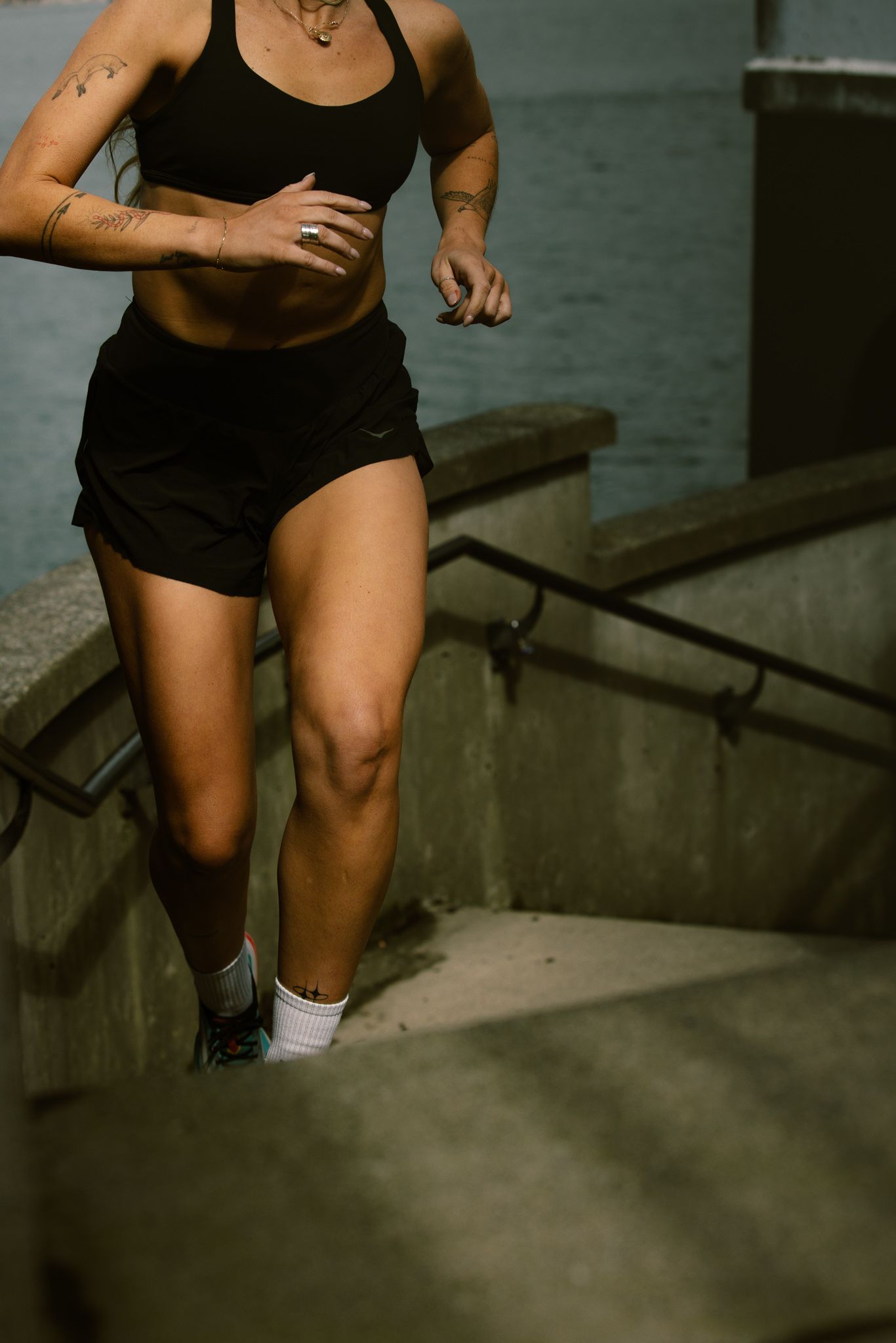 Athletic woman in black sports bra and shorts running up concrete stairs outdoors.