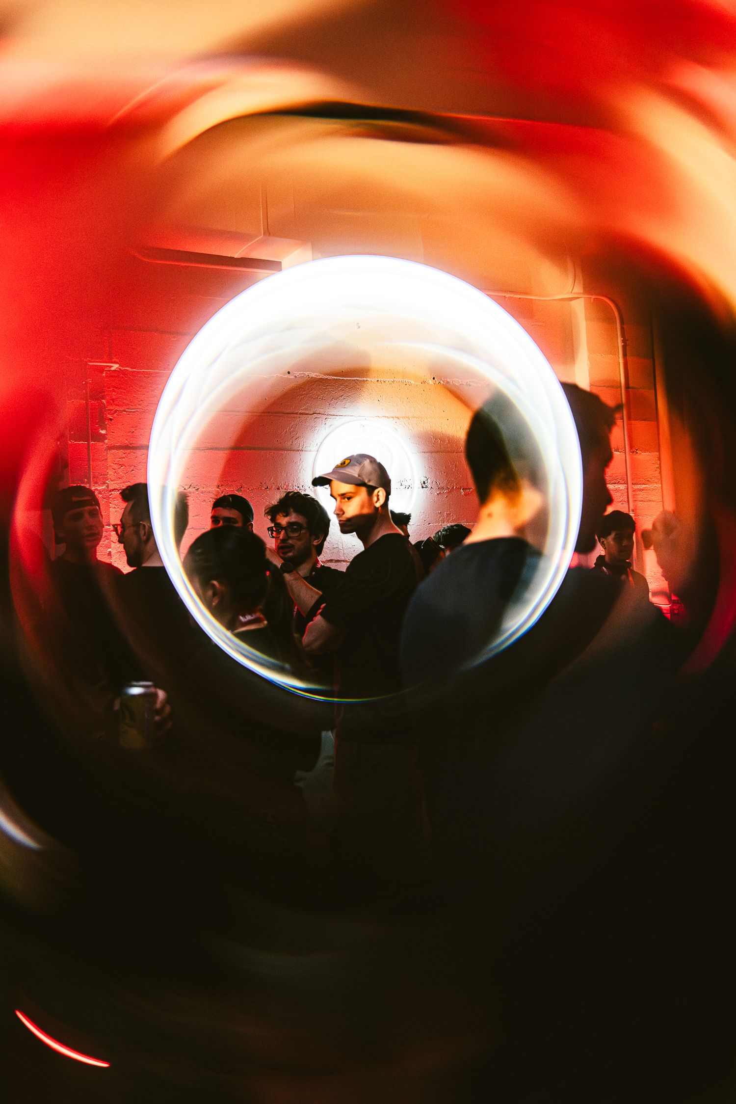 People gathered at a nightclub viewed through a circular lens with red ambient lighting and motion blur effects.