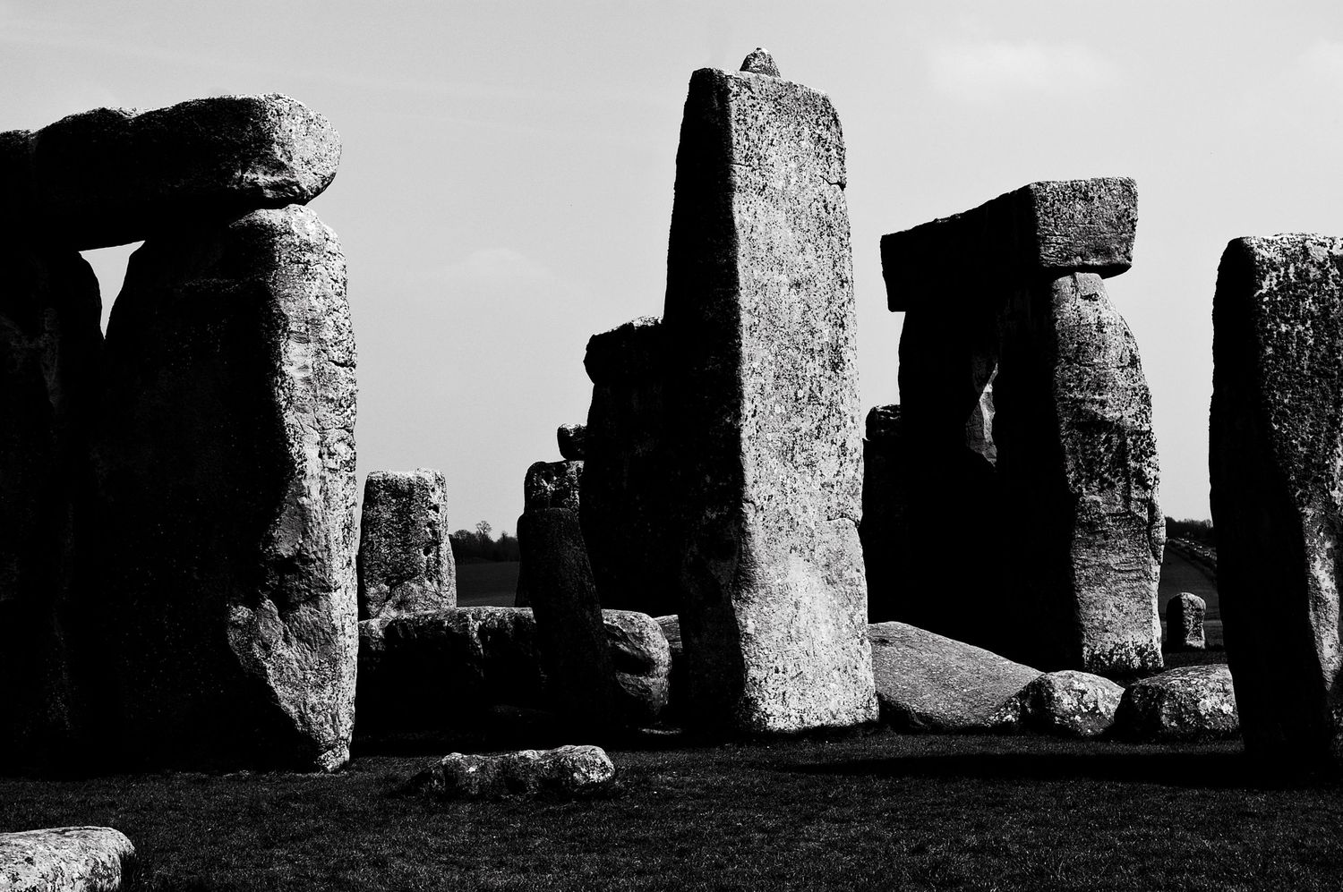 Black and white photo of ancient Stonehenge megalithic stone monument standing against a cloudy sky in Wiltshire, England.