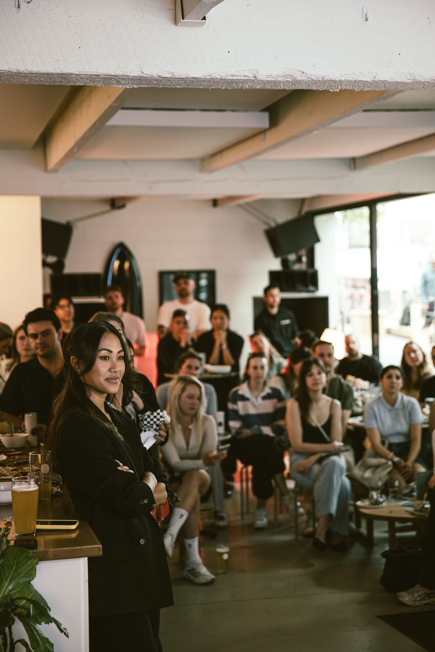 Woman in black blazer stands before an engaged audience at an indoor event or panel discussion.