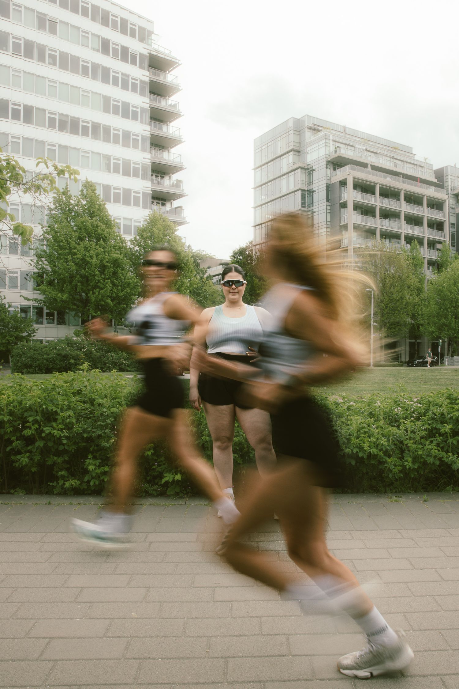 Motion blur captures runners in a city park during a race, with one athlete standing still among the movement.