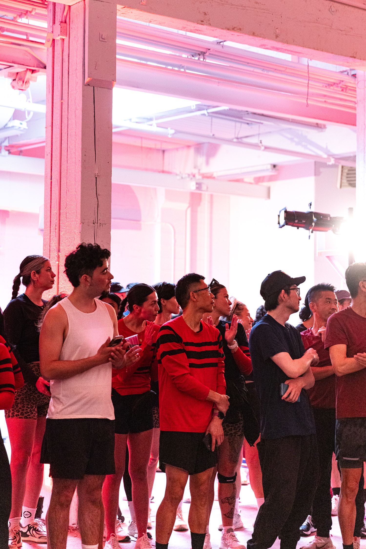 Group of athletes in red and black activewear gathered indoors under pink neon lights at a fitness event.