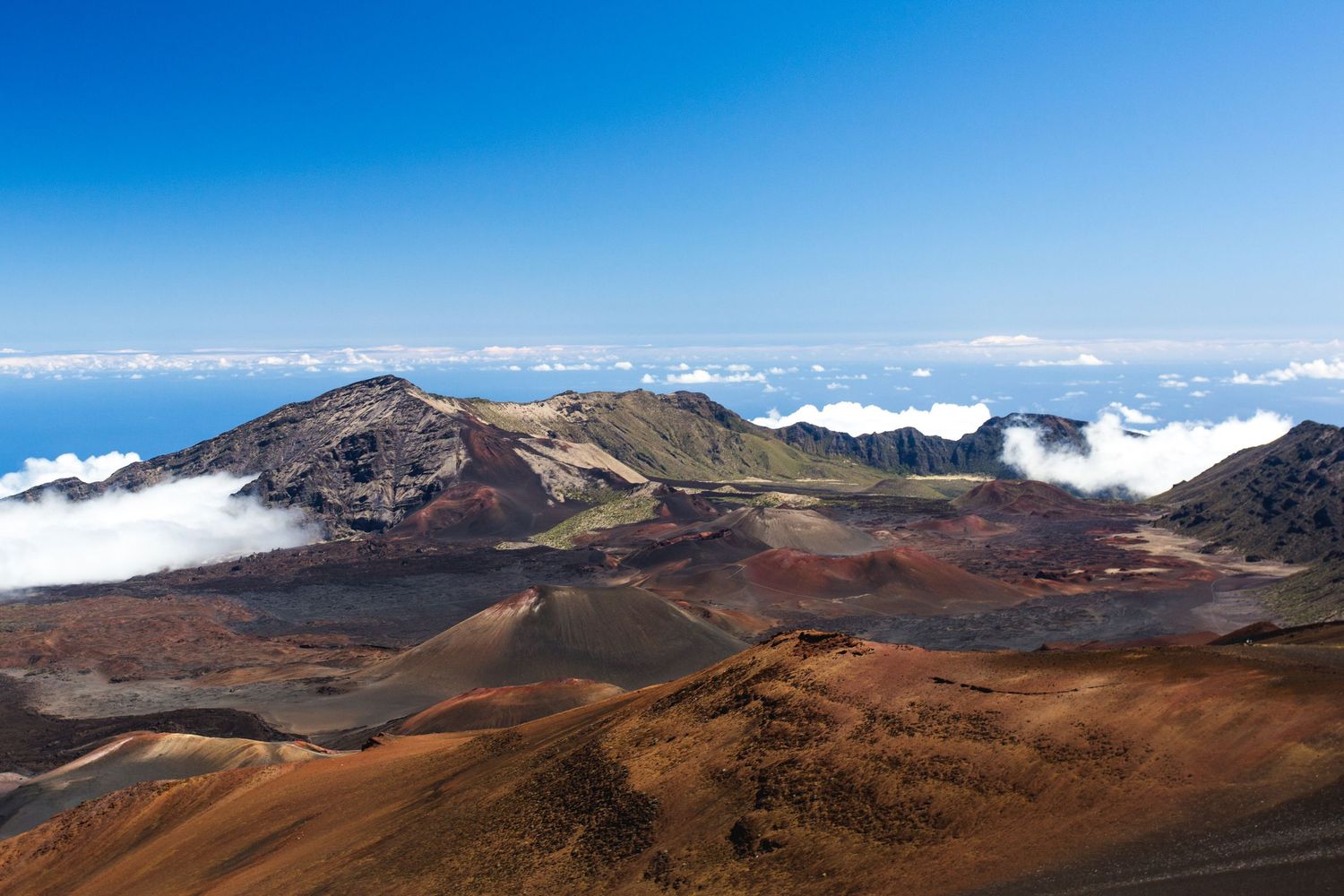 Aerial view of Haleakala volcanic crater in Maui, Hawaii, with colorful cinder cones and clouds below the summit.
