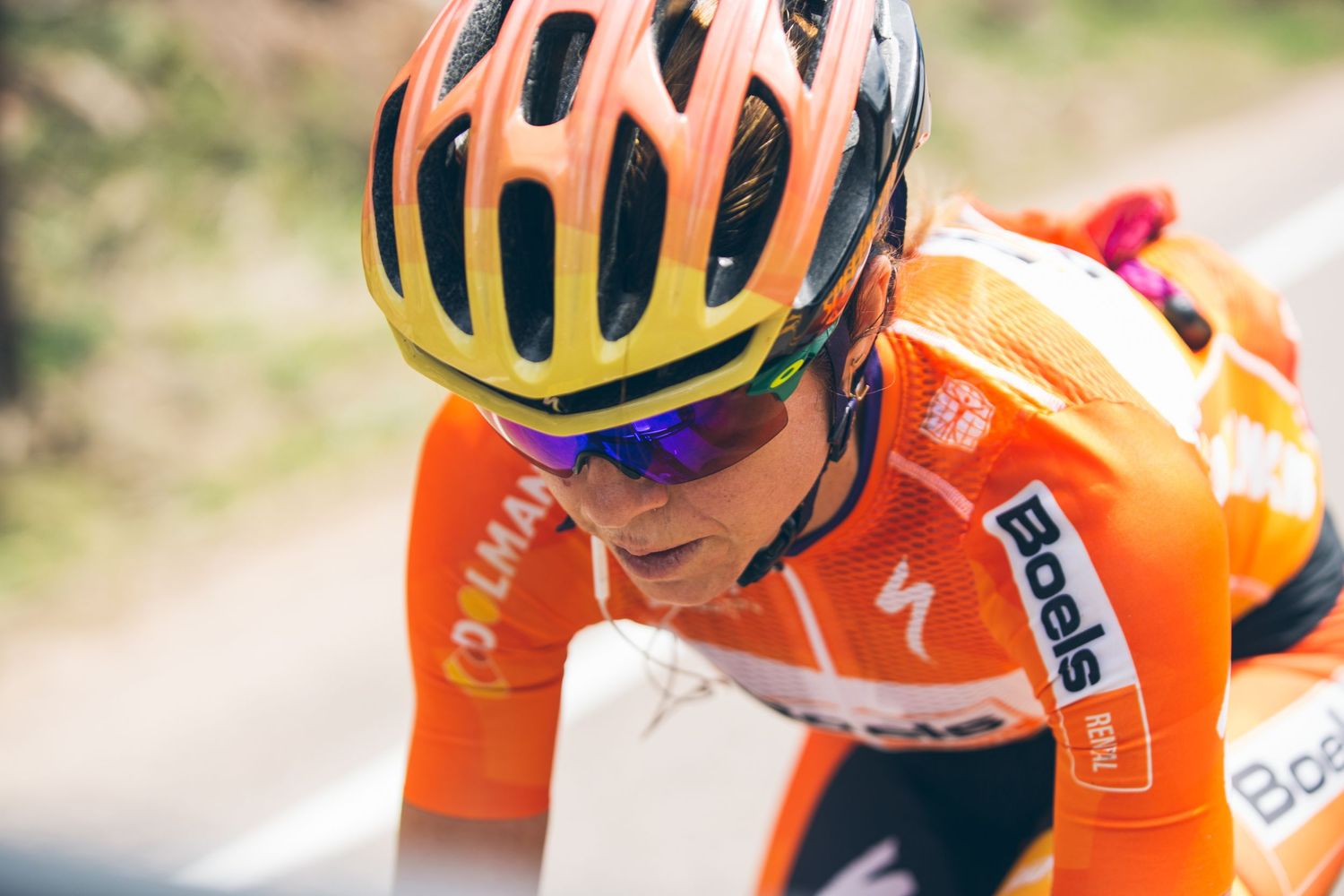 Cyclist in orange Boels team jersey and yellow helmet rides intensely during a professional road cycling race.