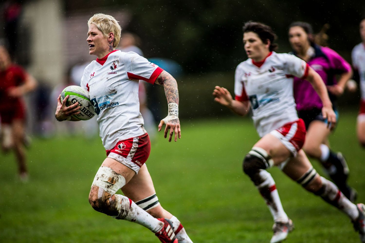 Women rugby players in white and red uniforms compete during an outdoor match, with one player running with the ball.