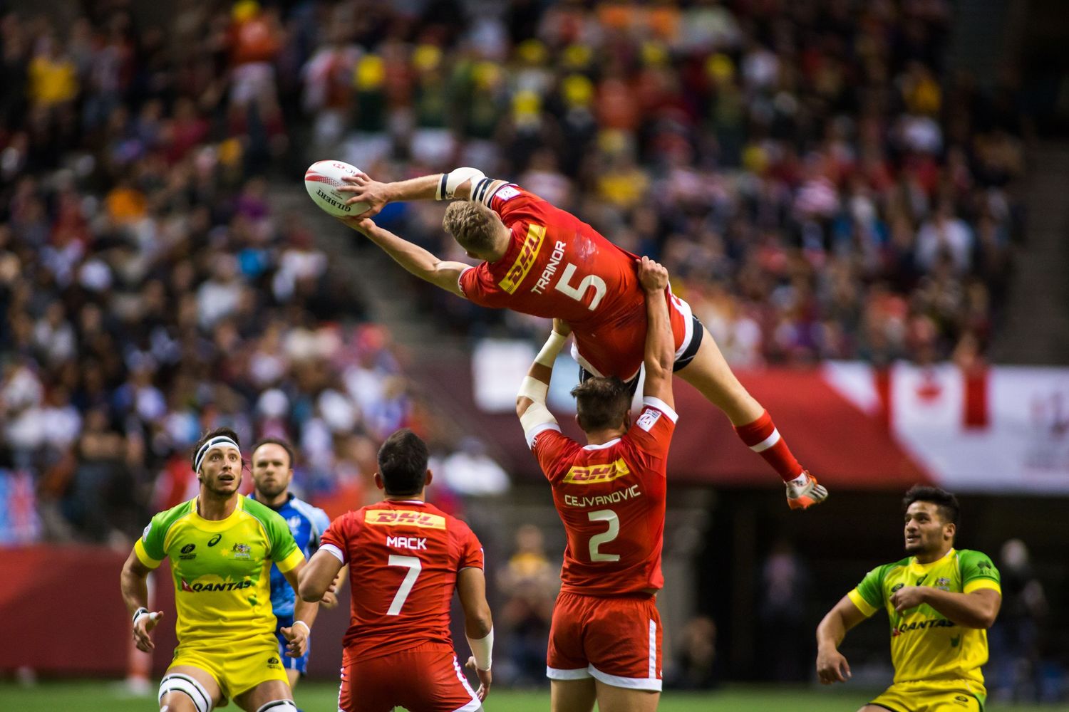 Canada rugby player lifted by teammates catches ball in lineout during intense match against Australia at indoor stadium.