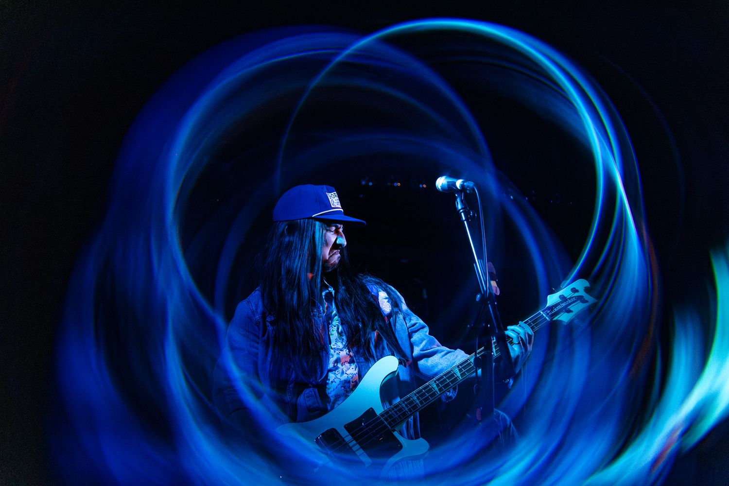 Guitarist and vocalist on stage surrounded by vivid swirling blue light trails in a long-exposure concert photo.