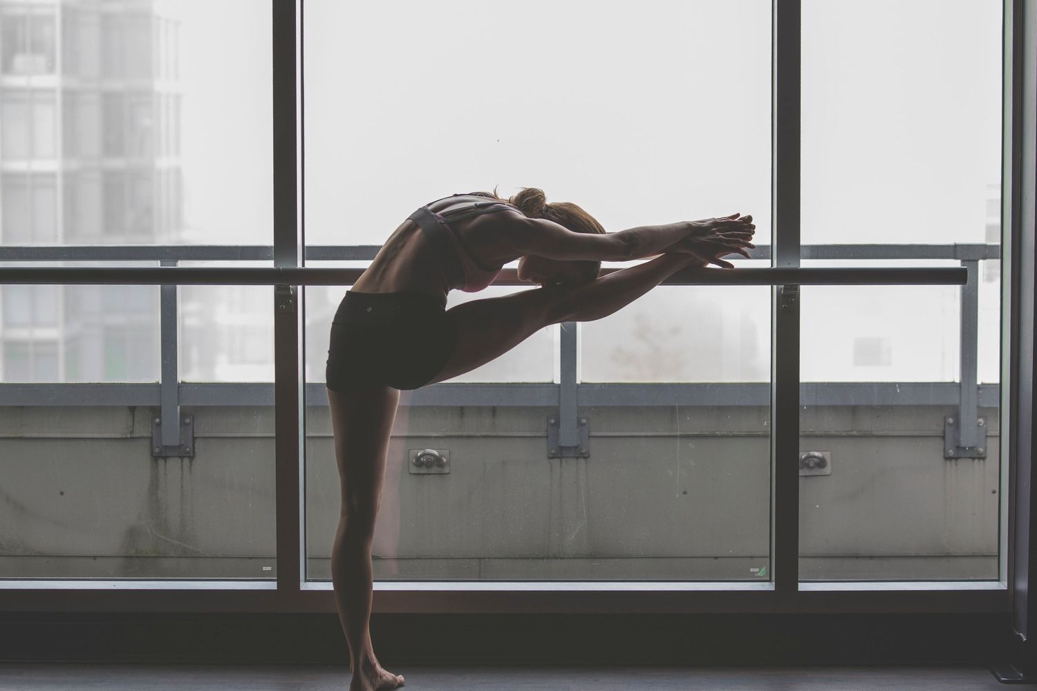 Flexible dancer performing a deep backbend stretch in a bright studio with large windows.