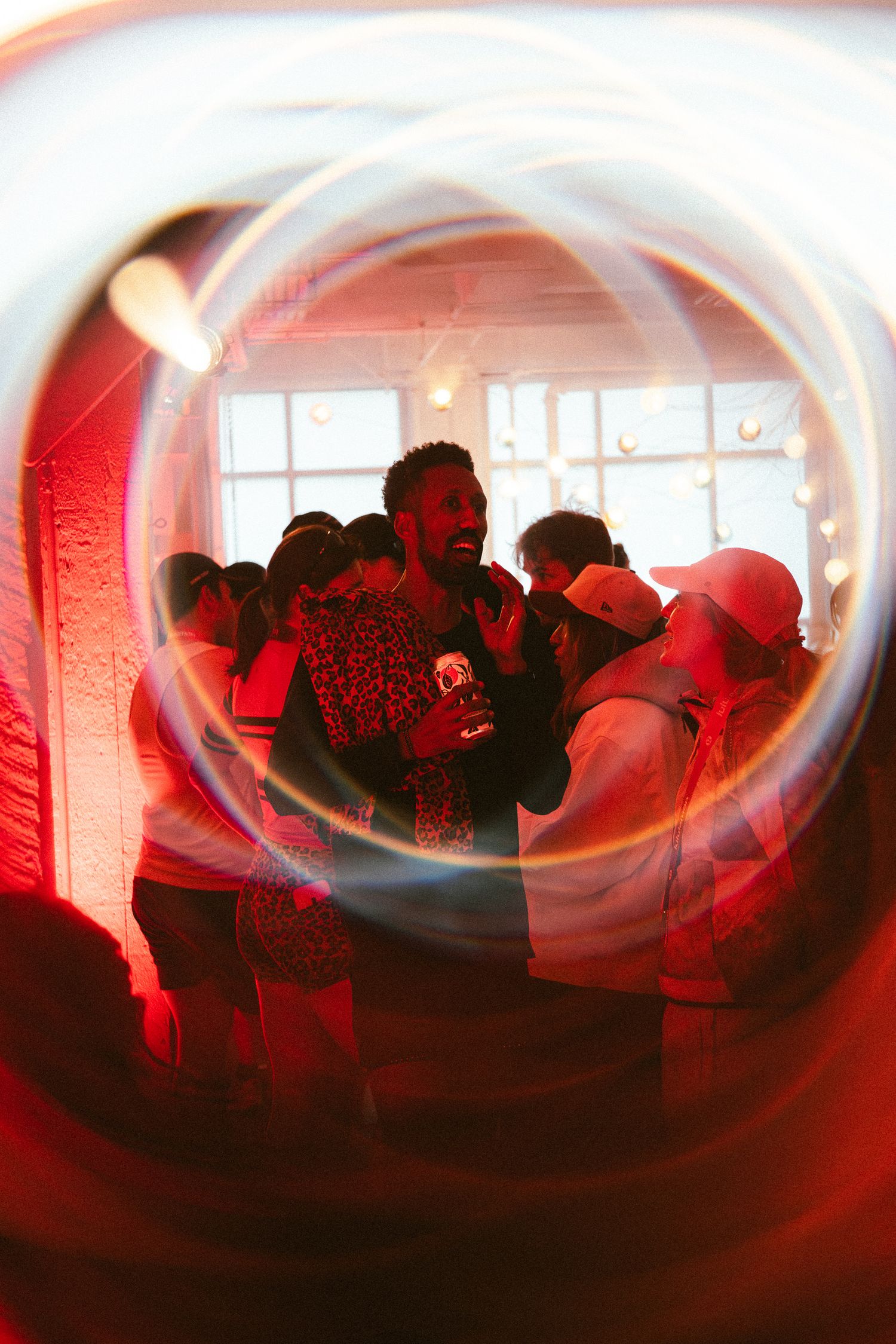 Group of people socializing at a vibrant red-lit party, captured through a swirling light effect lens.