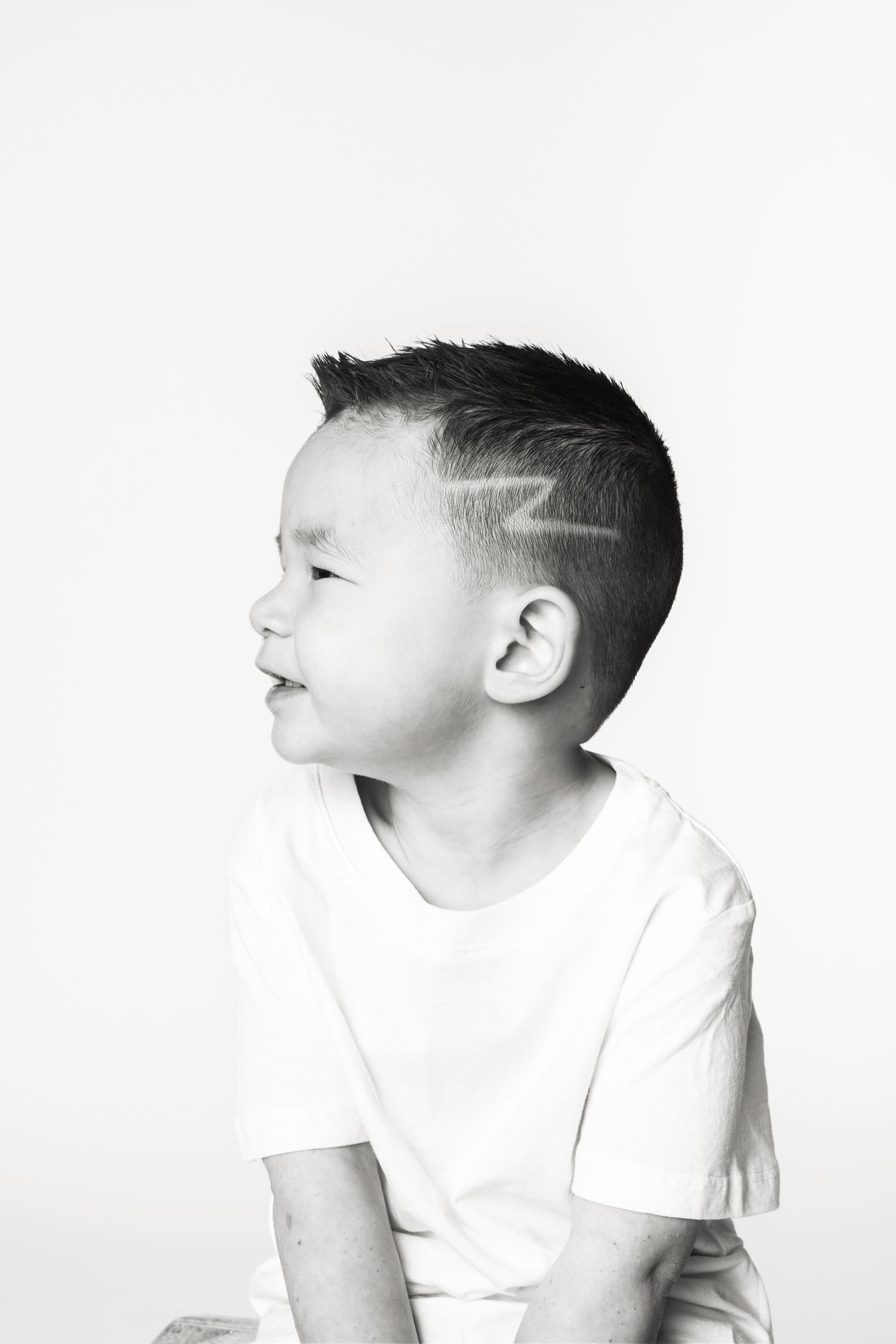 Black and white portrait of a smiling young boy with a lightning bolt haircut design shaved into his hair.