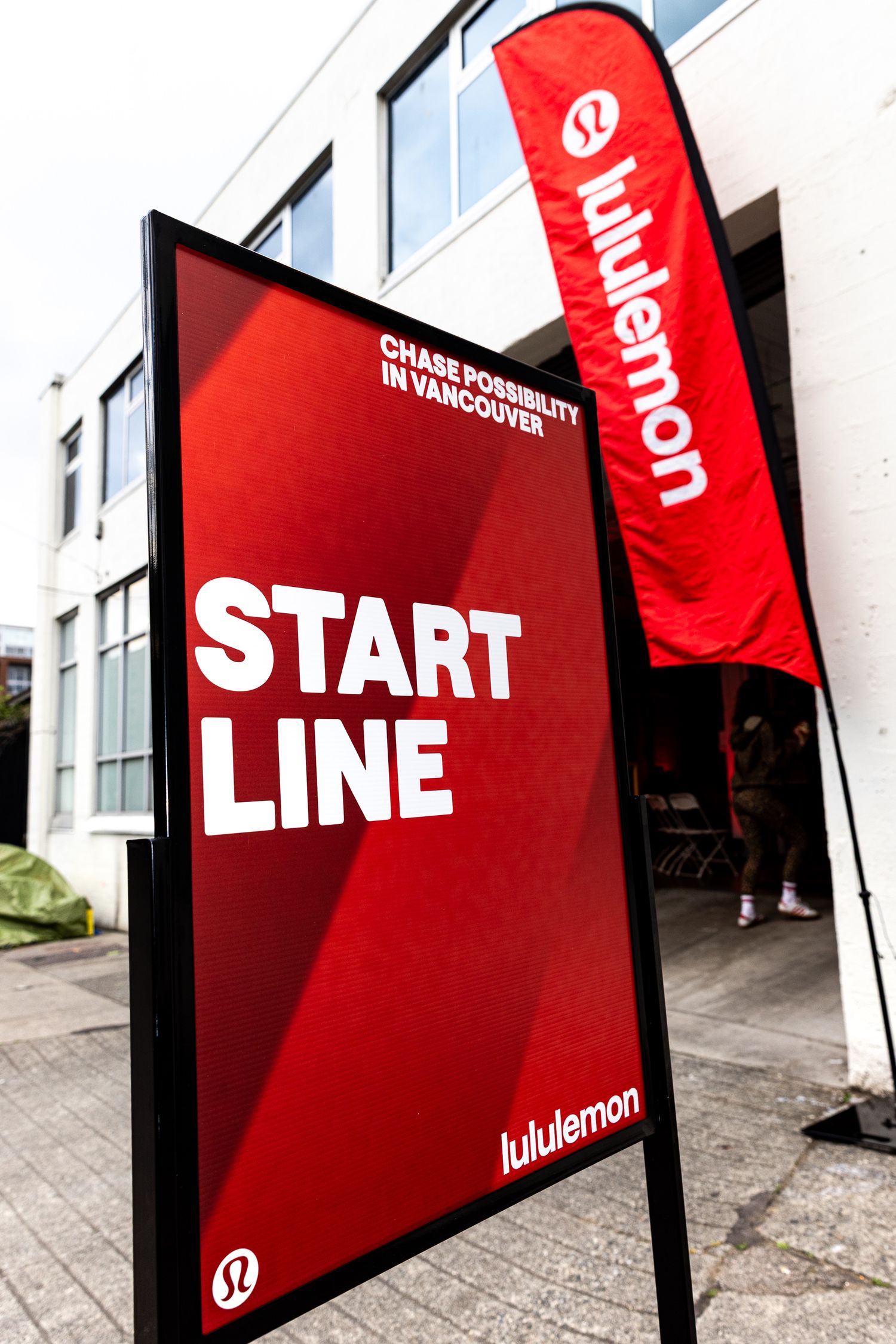 Lululemon red START LINE sign at Chase Possibility event in Vancouver, with branded flag banner outside store.