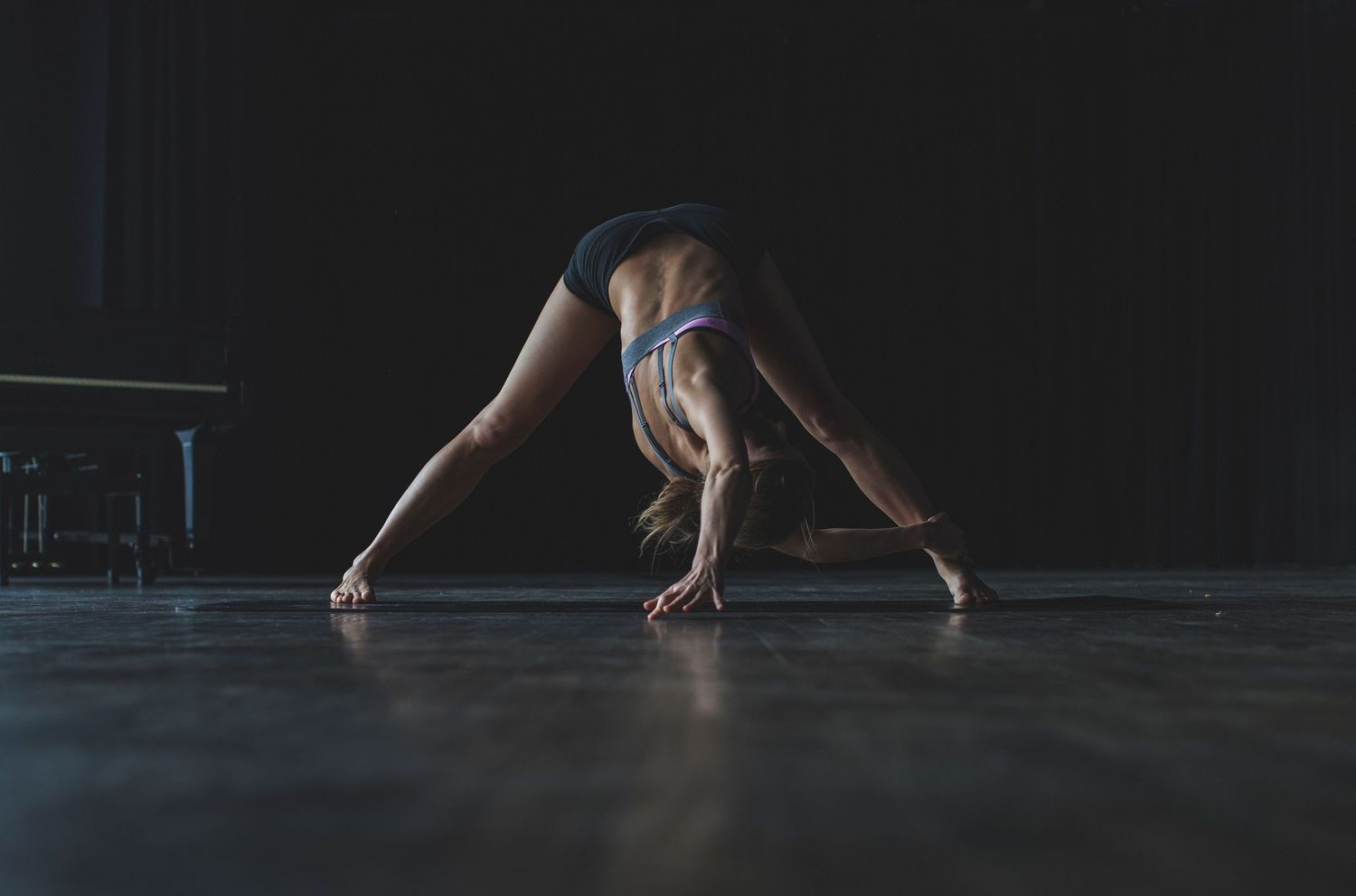 Flexible dancer in blue shorts performs a deep forward bend on a dark studio floor.