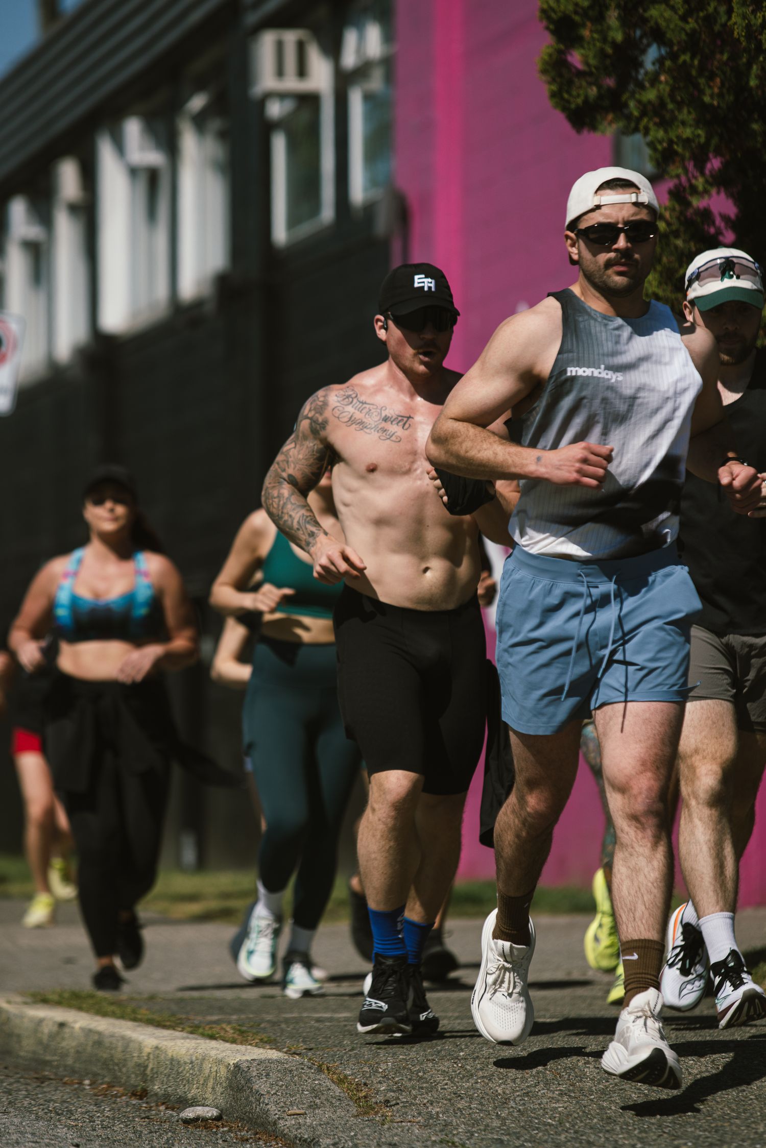 Group of runners jogging down a sunny urban street past a pink building during an outdoor fitness event.