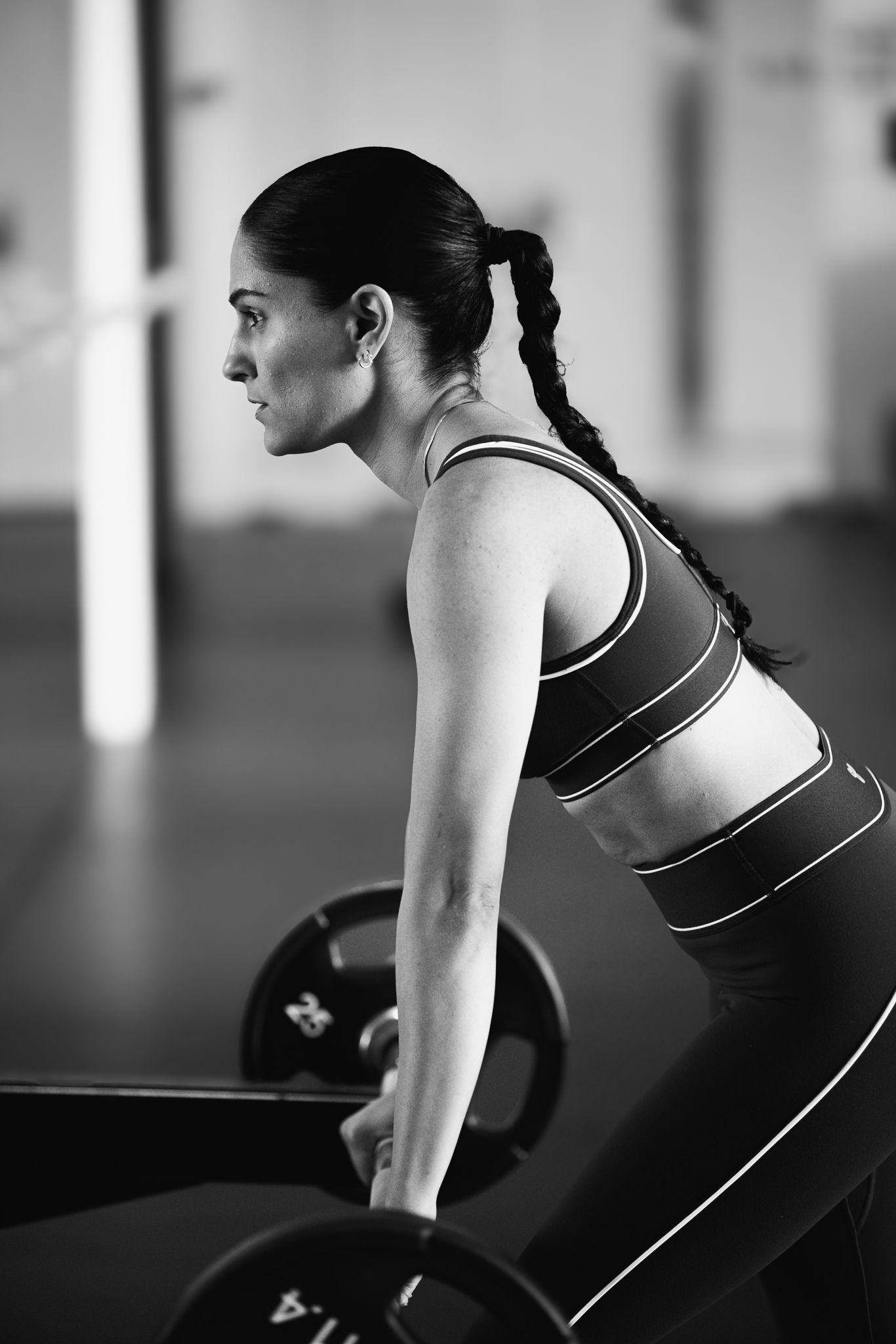Athletic woman in sports bra preparing to deadlift barbell in black and white gym photo.
