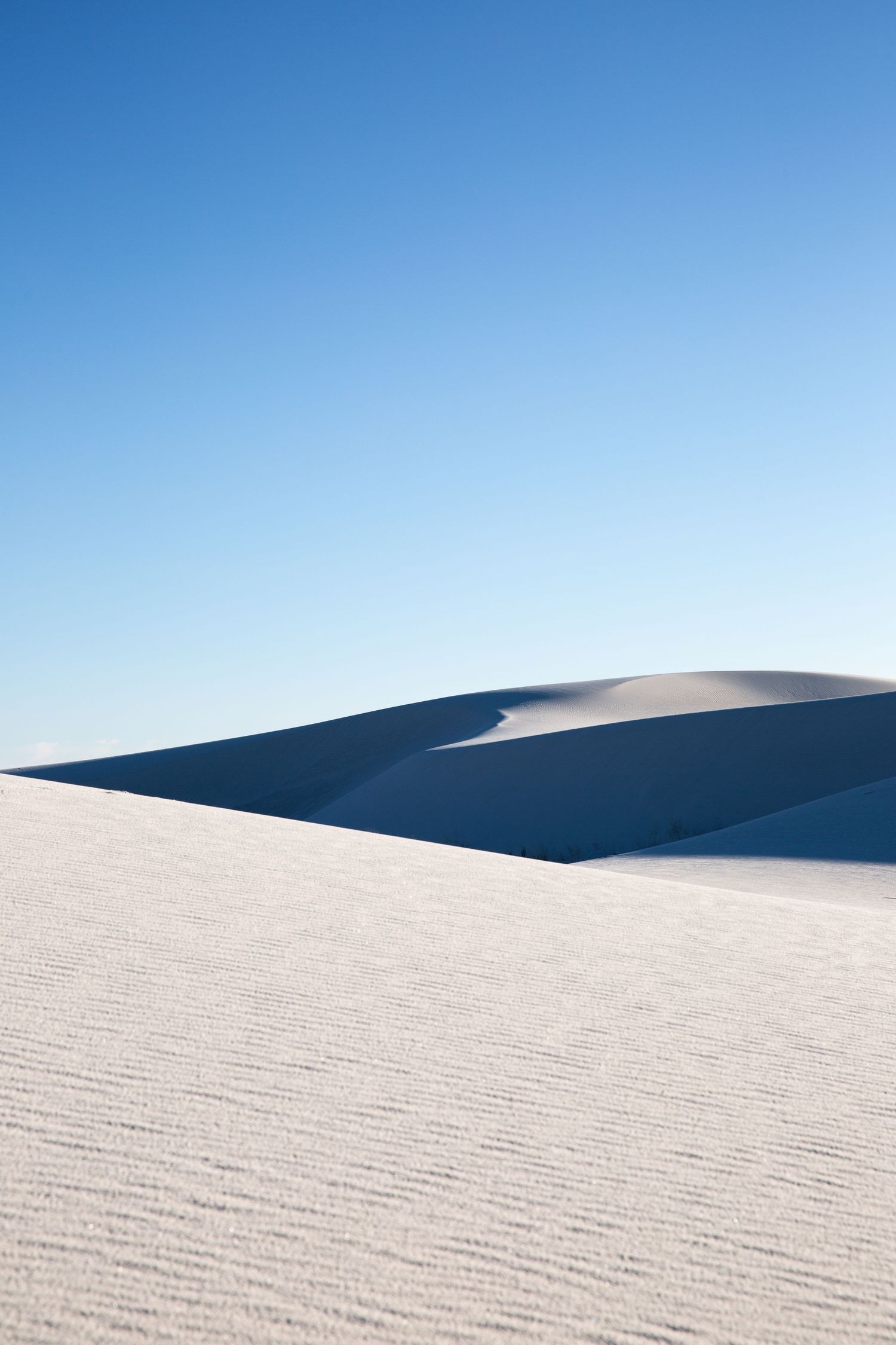 White sand dunes under a clear blue sky at White Sands National Park, New Mexico, USA.