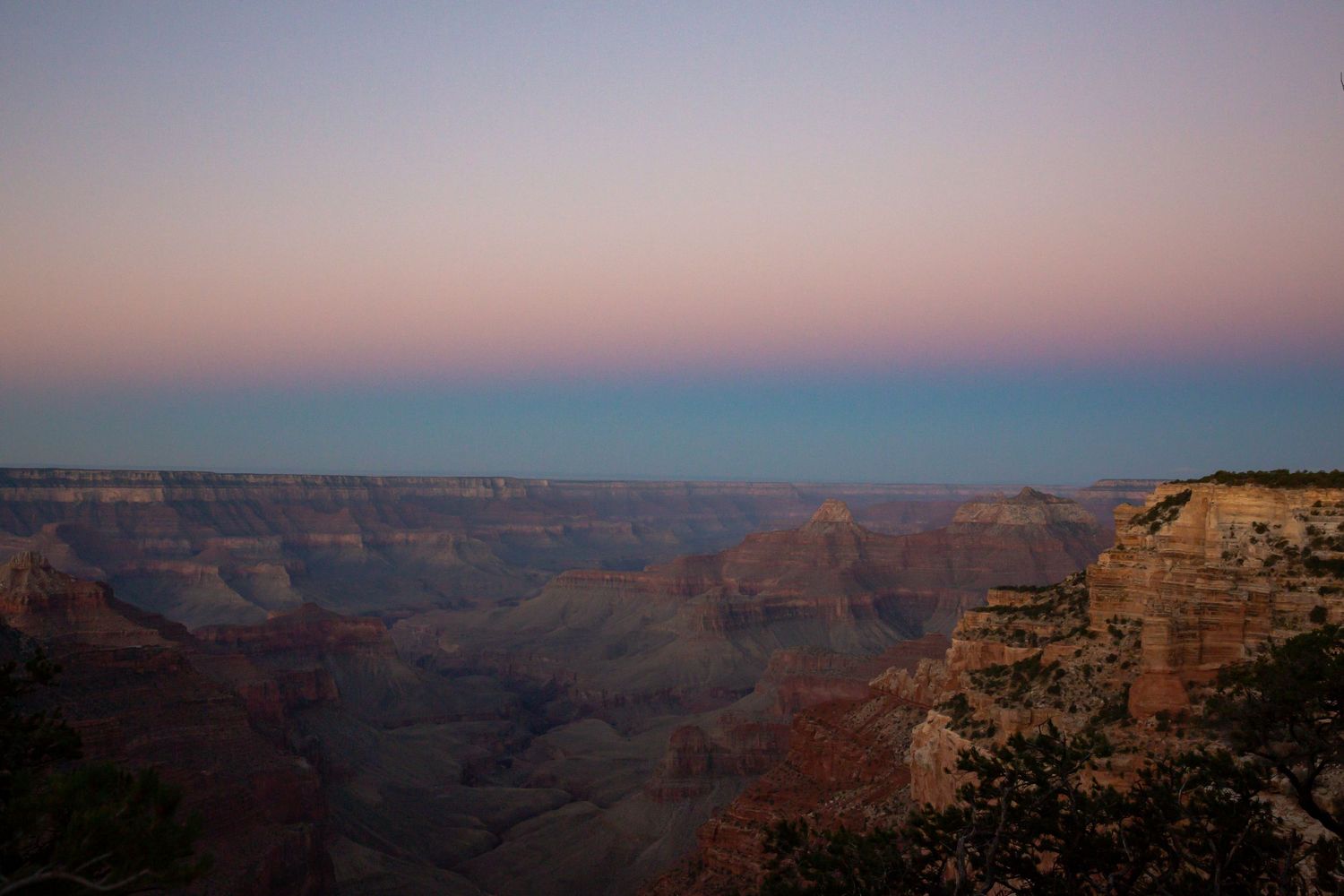 Stunning twilight view of the Grand Canyon with pink and blue sky gradients illuminating the vast layered rock formations.