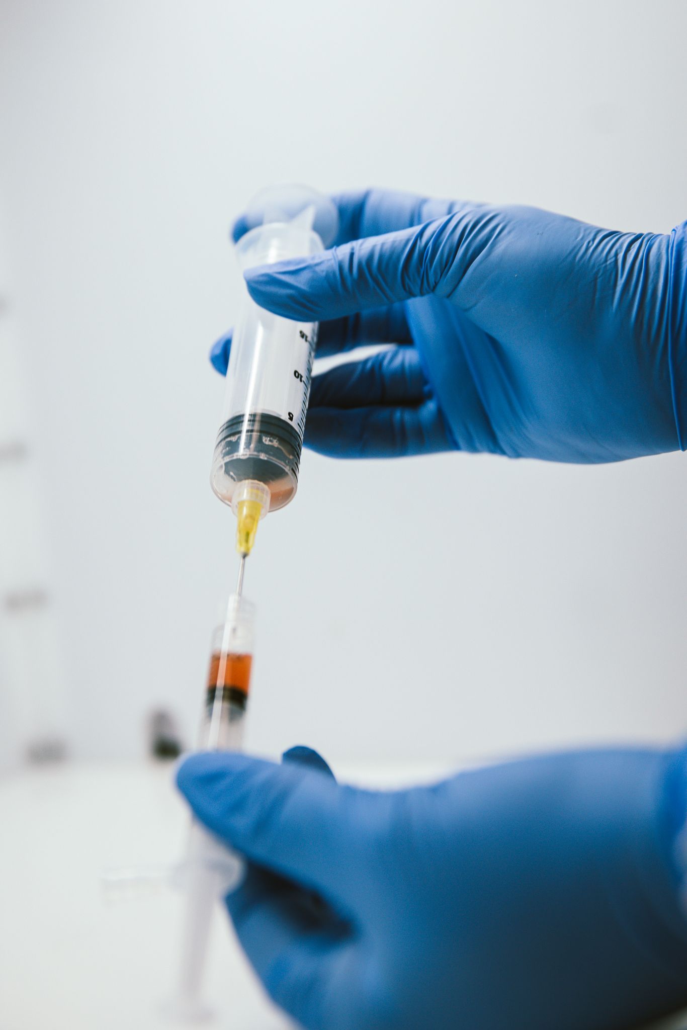Medical professional in blue gloves transfers golden-colored liquid between syringes in a clinical setting.