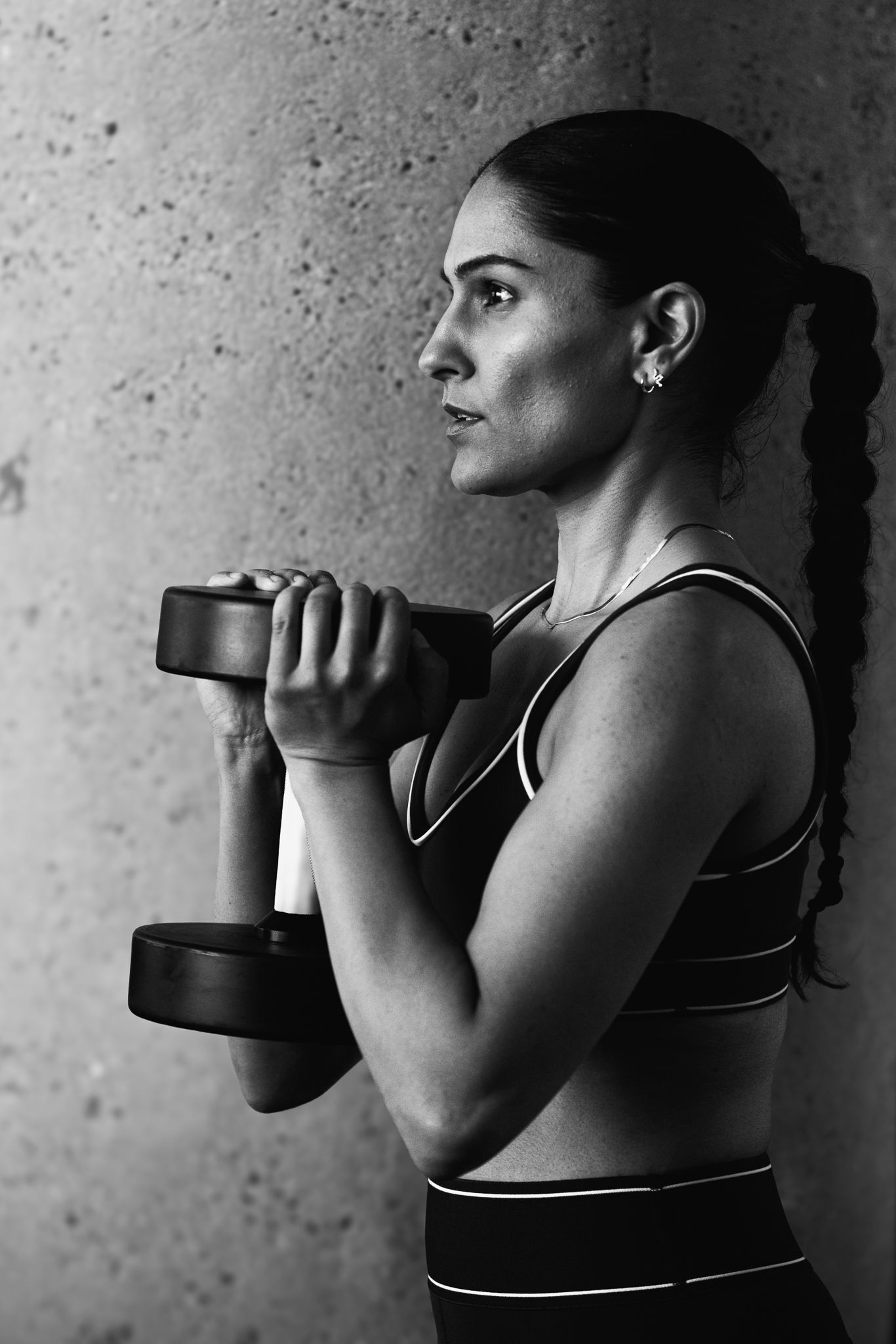 Athletic woman lifting dumbbells in a black and white fitness portrait.