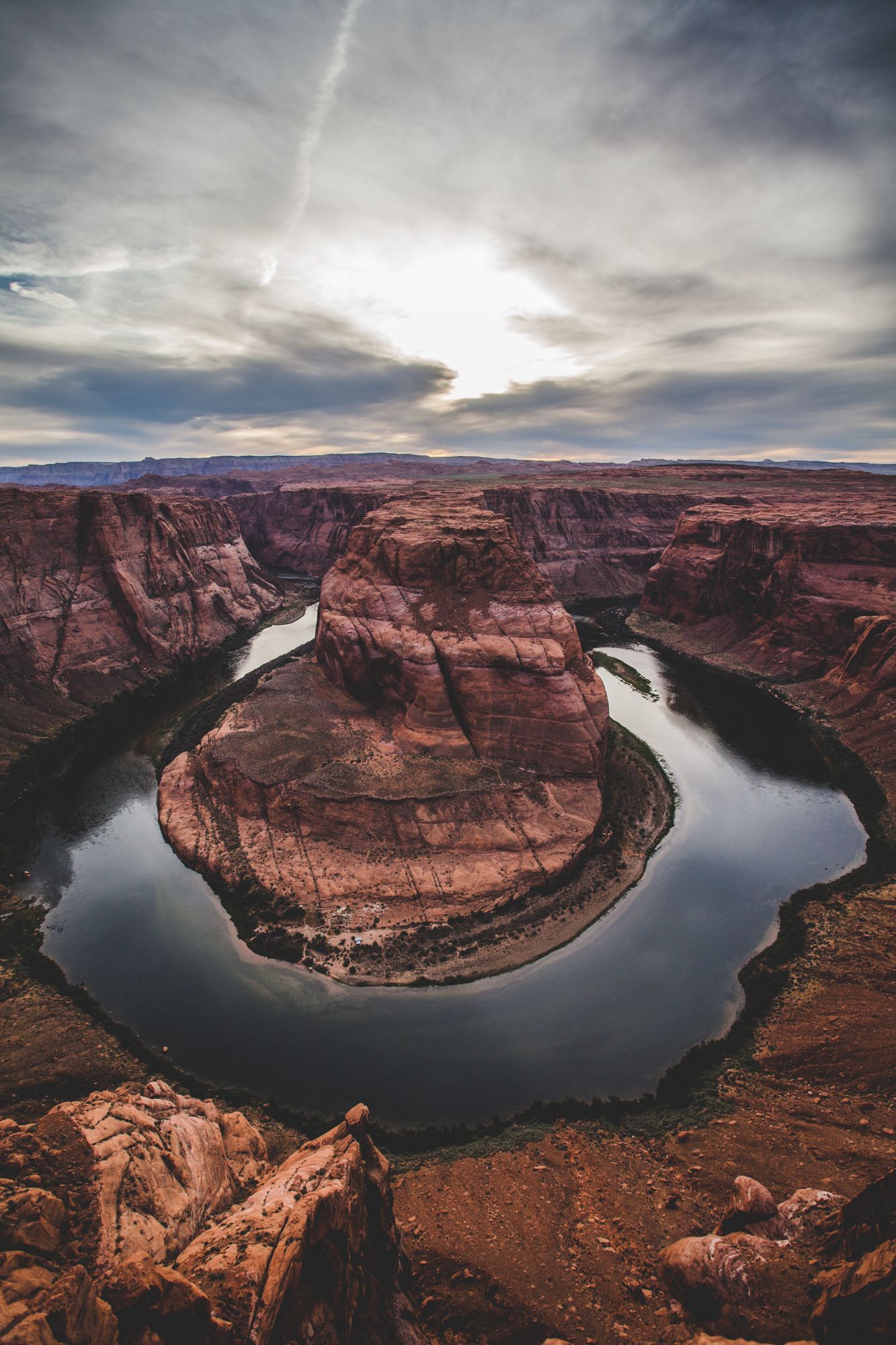 Aerial view of Horseshoe Bend, a dramatic Colorado River meander curving around red sandstone cliffs under a cloudy sky.