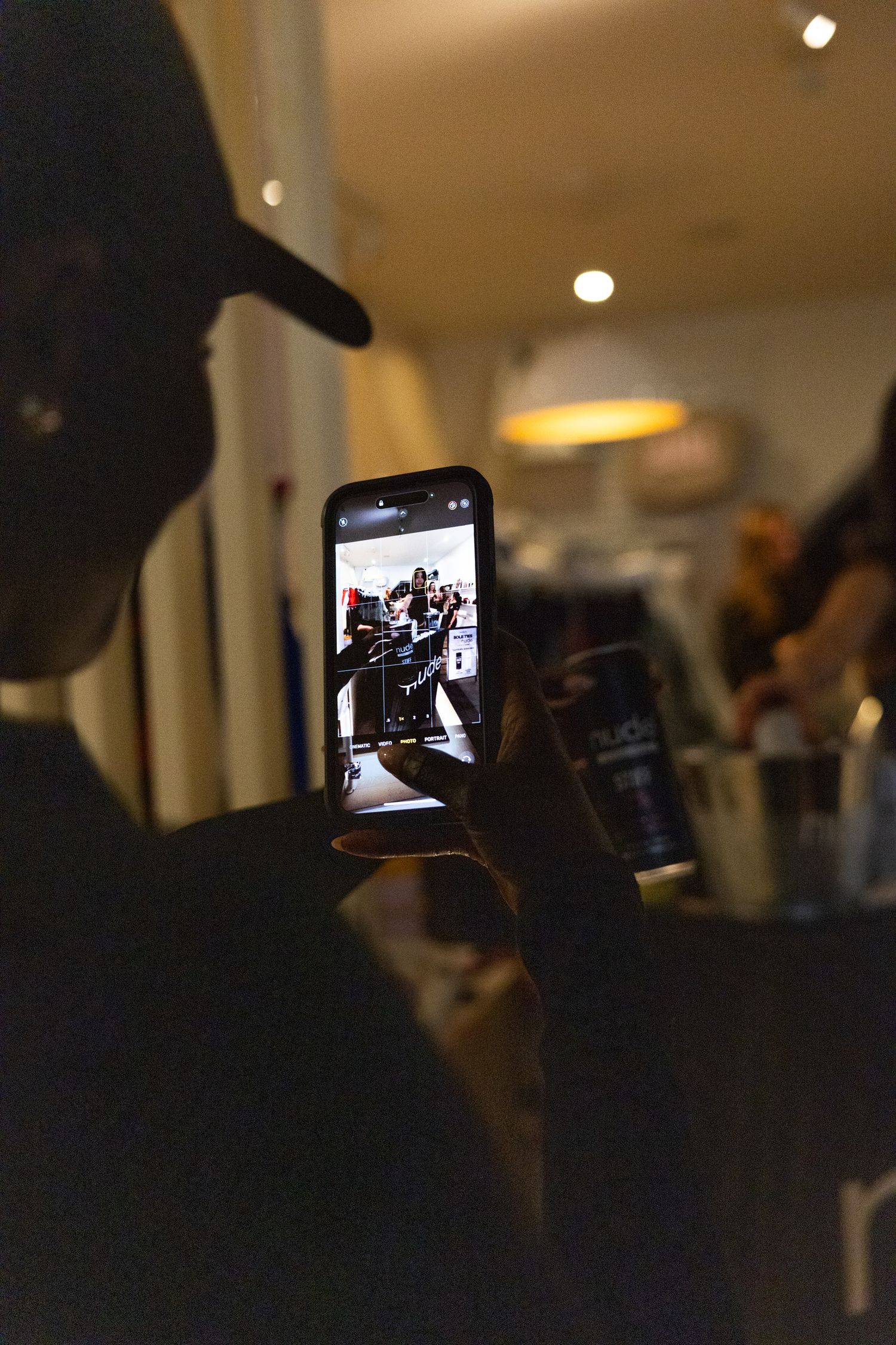 Silhouetted person films live event on smartphone in dimly lit indoor venue.
