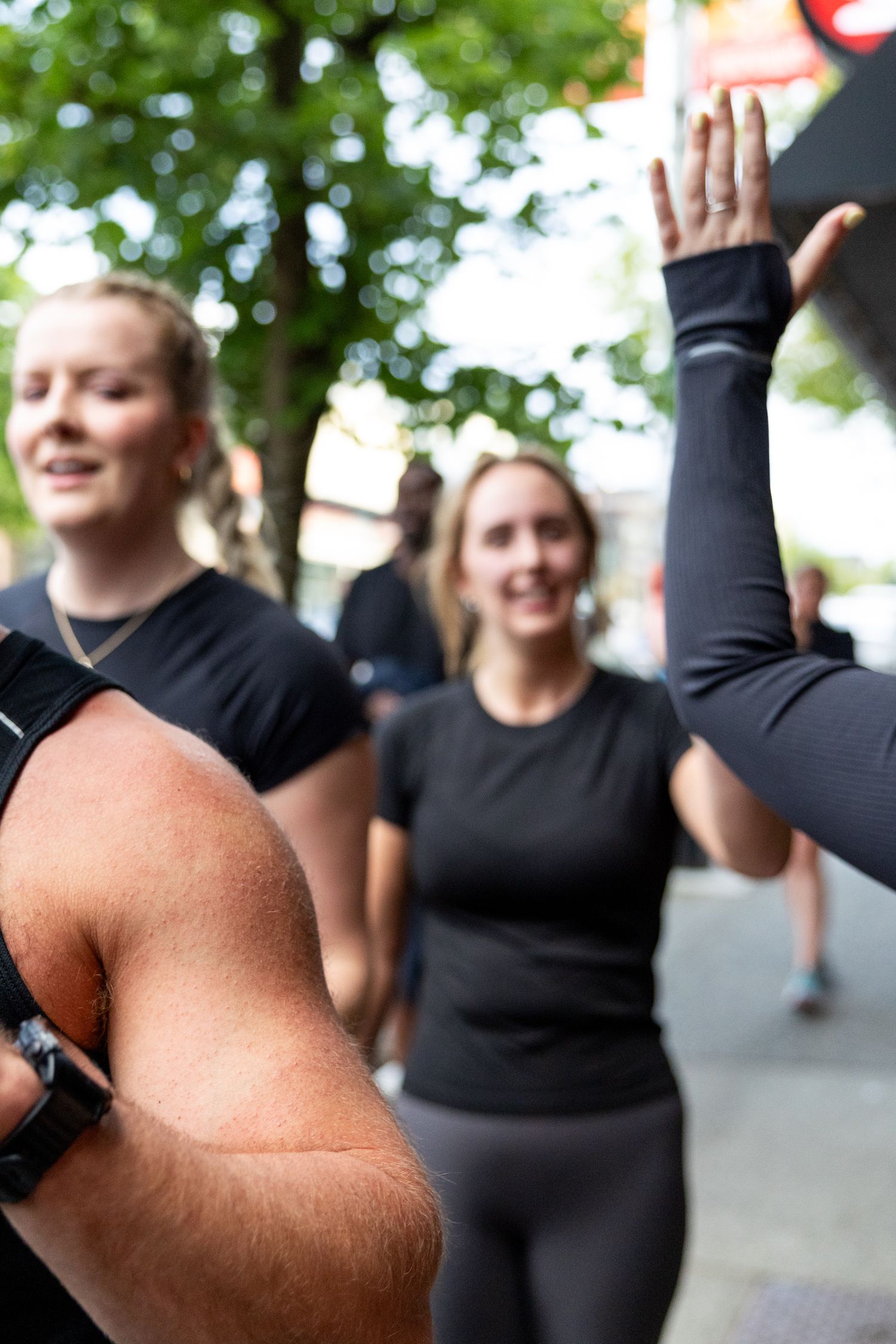 Two women in black athletic wear smile while giving a high five outdoors after a workout session.